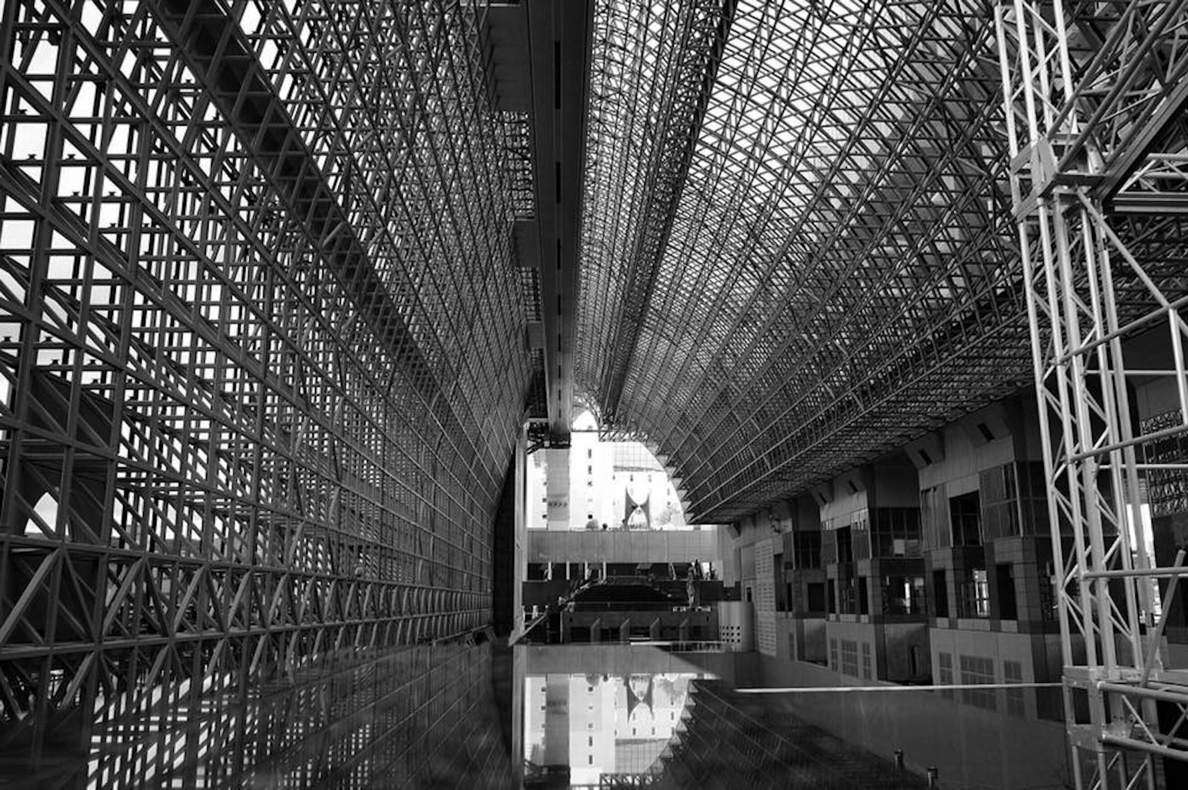 Monochrome photo showcasing the interior of a large structure featuring steel frames and a reflective floor