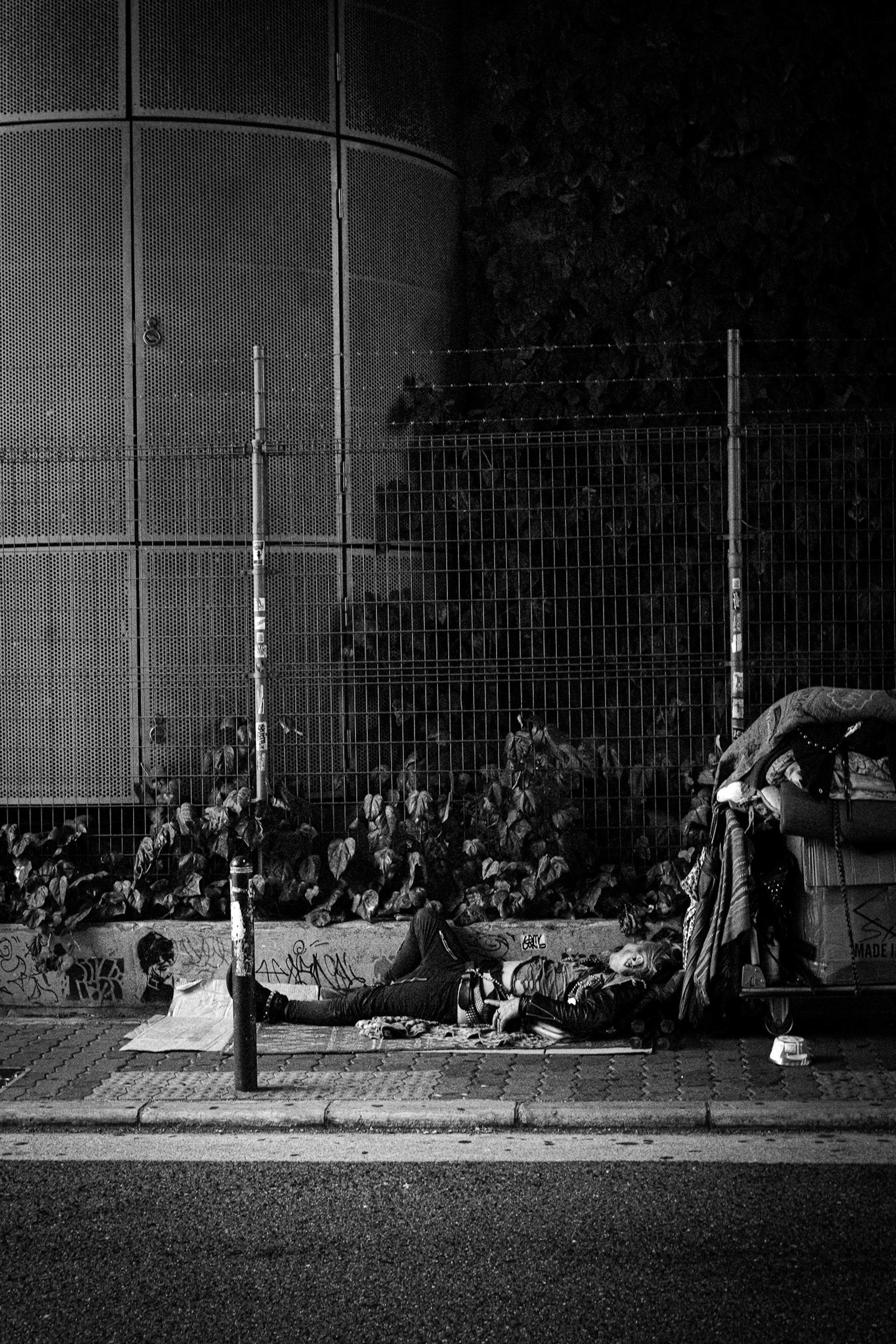 Homeless individuals lying on the street near a fence and garbage