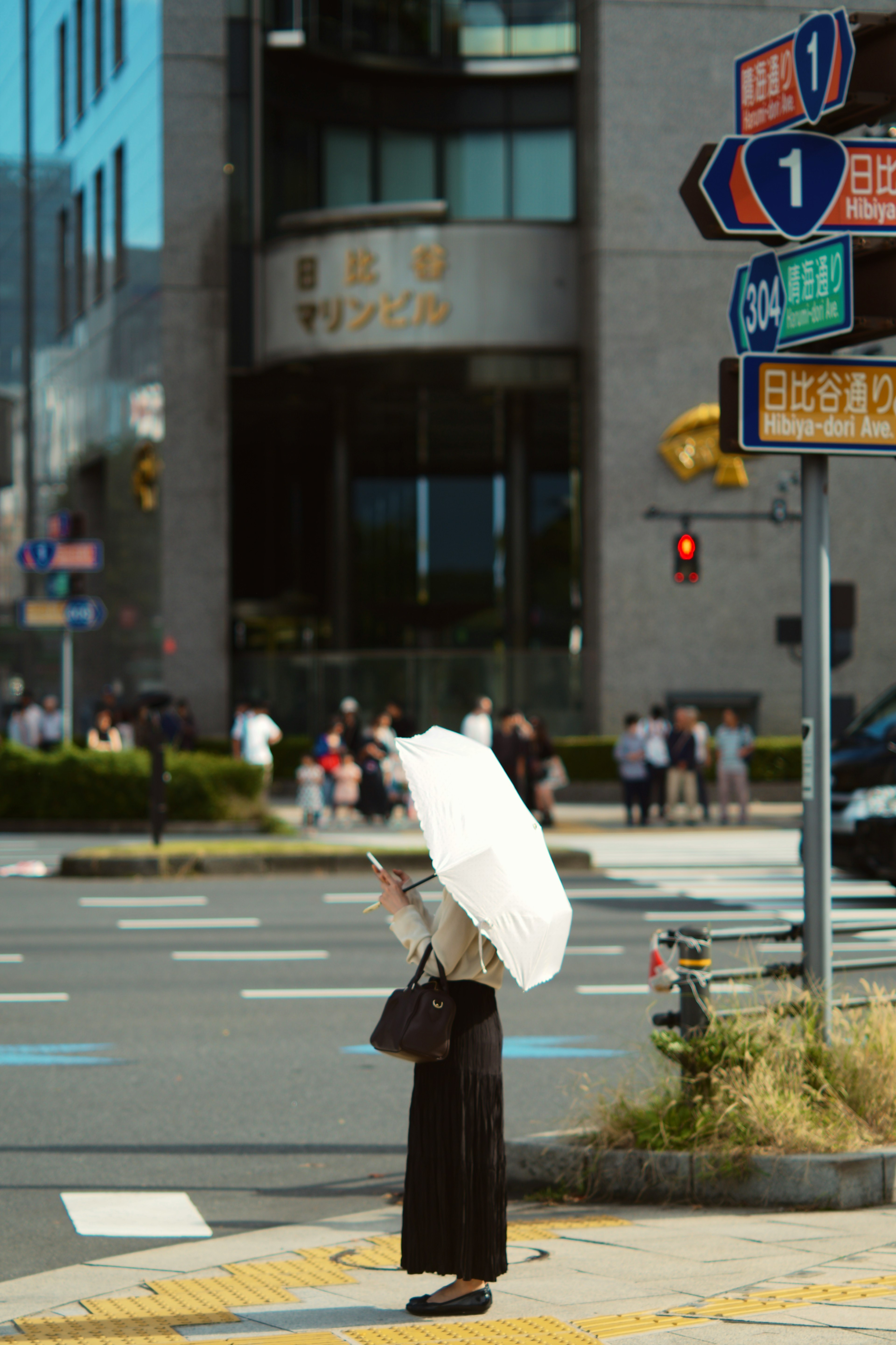 A woman holding a white umbrella waiting at an intersection in an urban setting