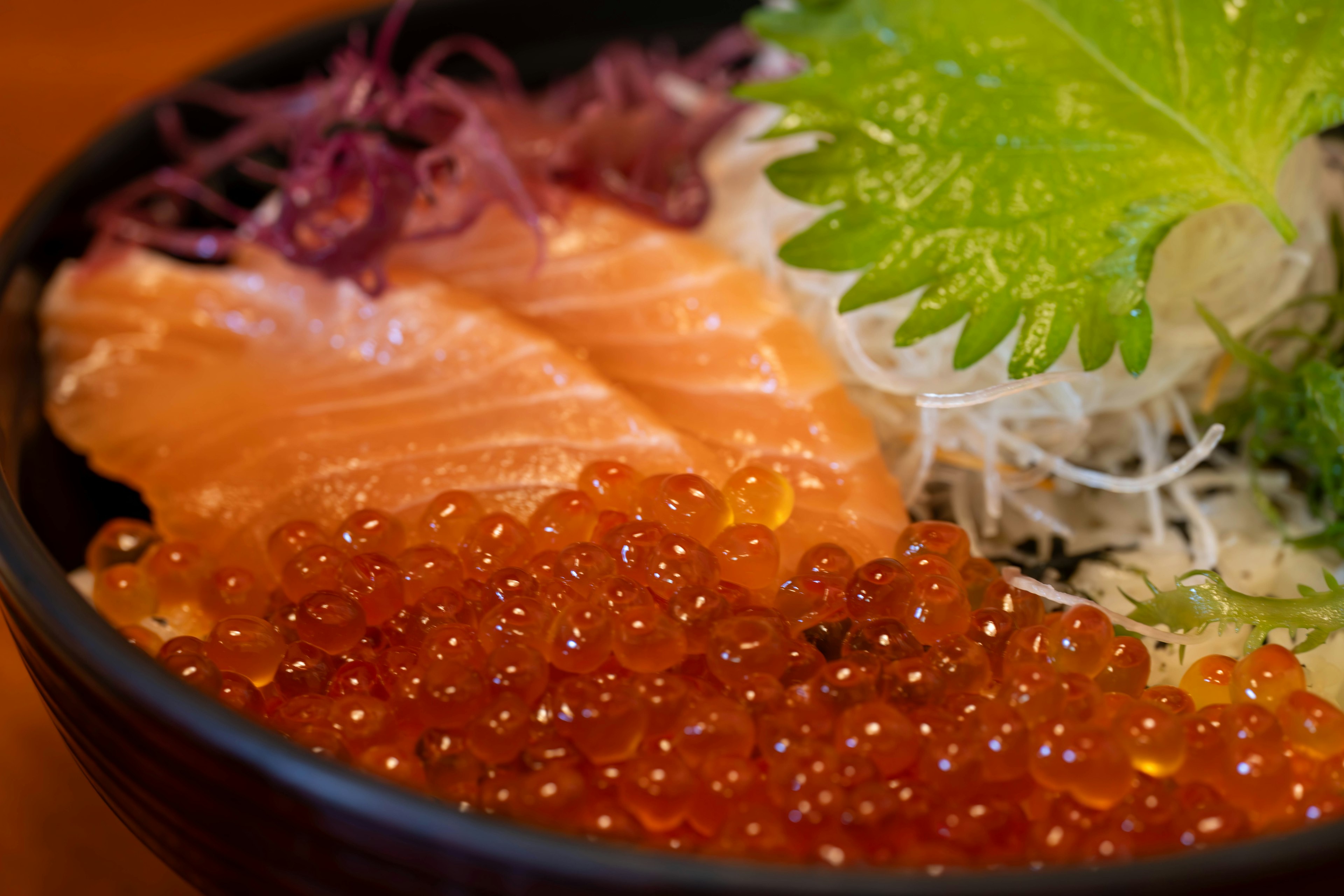 Bowl of salmon and ikura garnished with fresh vegetables