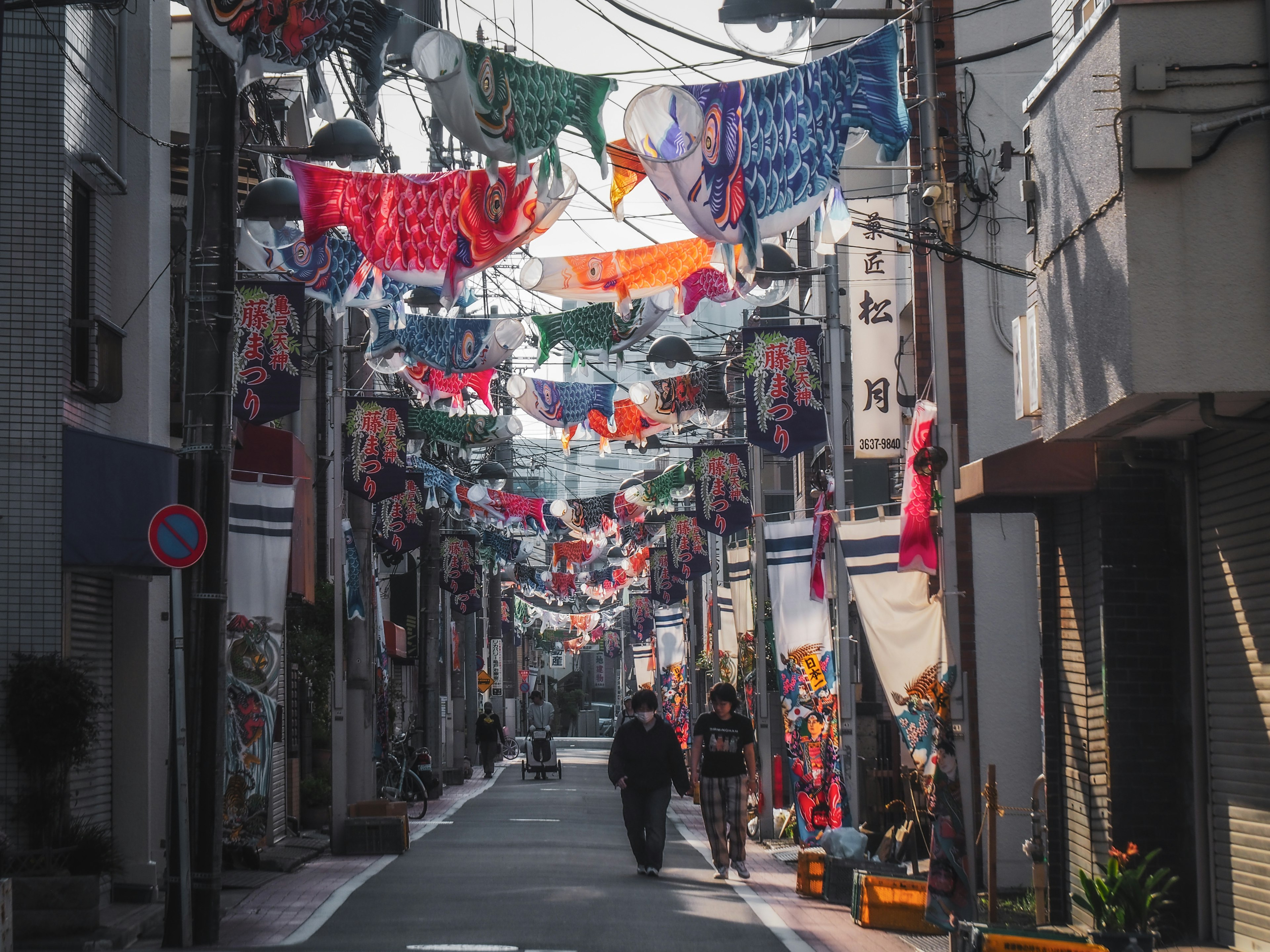 兩個人走在狹窄的街道上，街道上掛滿了五彩繽紛的旗幟