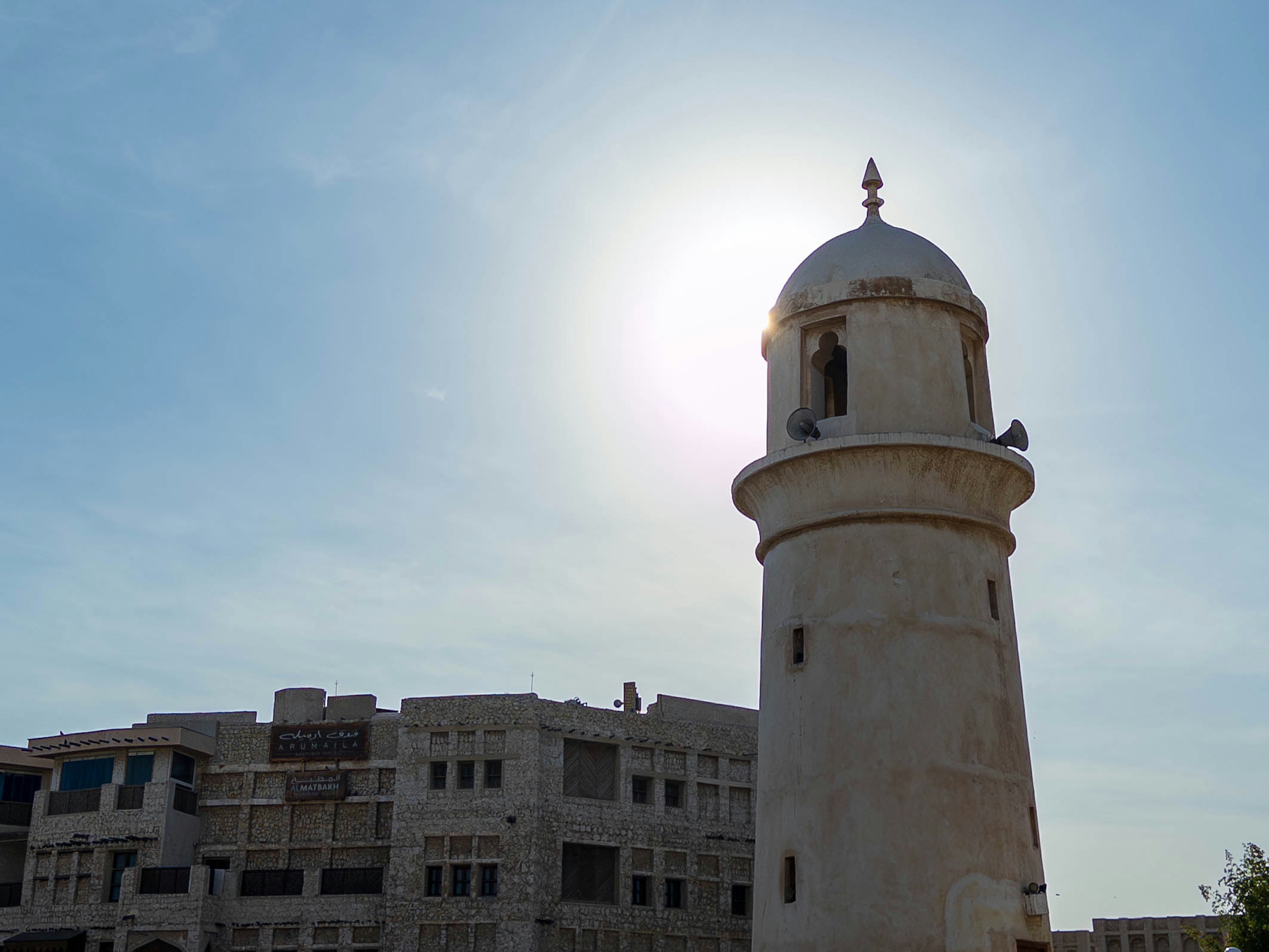 Tour blanche silhouettée contre le ciel bleu avec un ancien bâtiment à proximité