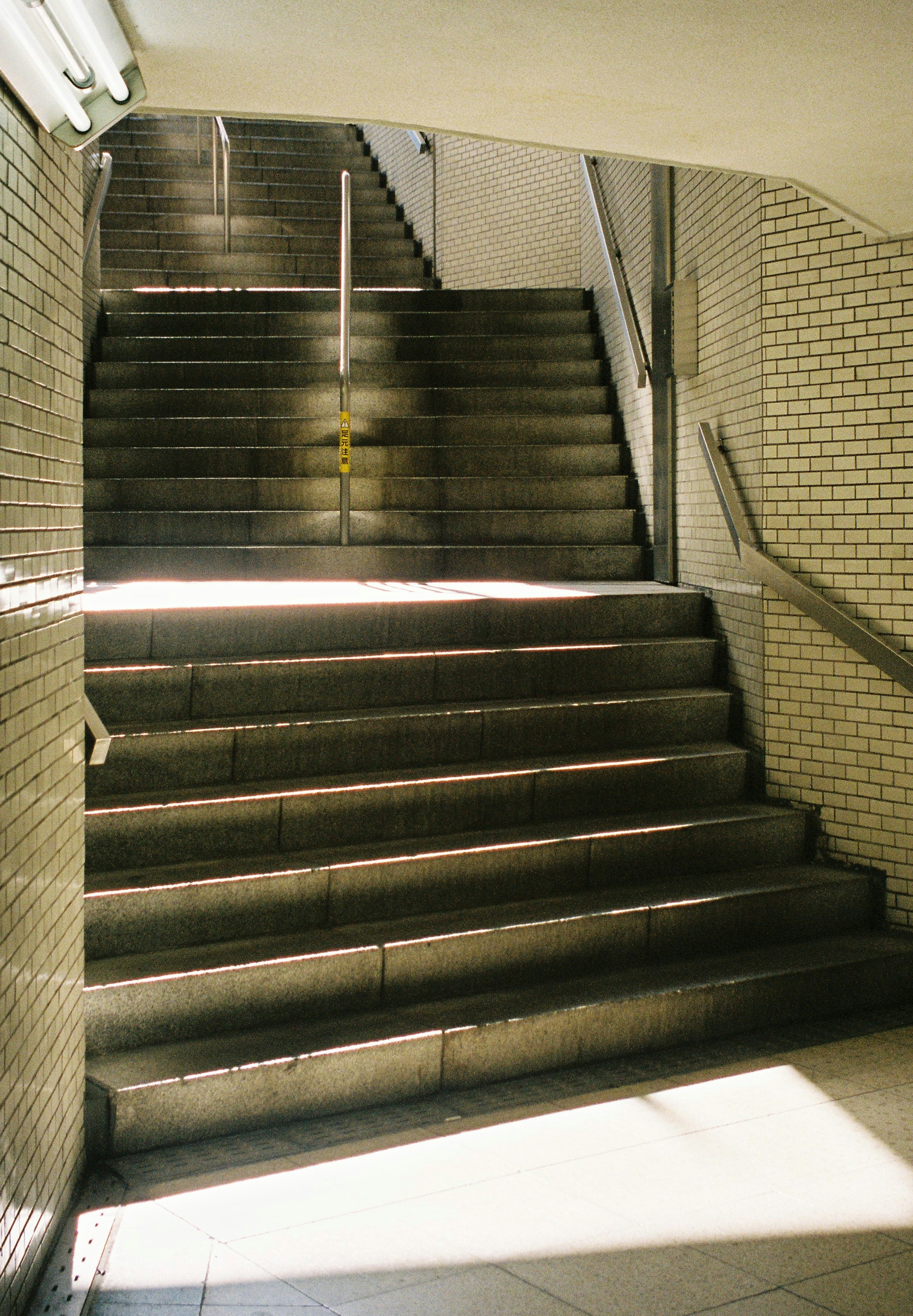 Escena de una escalera con luz brillando a través de los escalones de piedra y paredes de azulejos