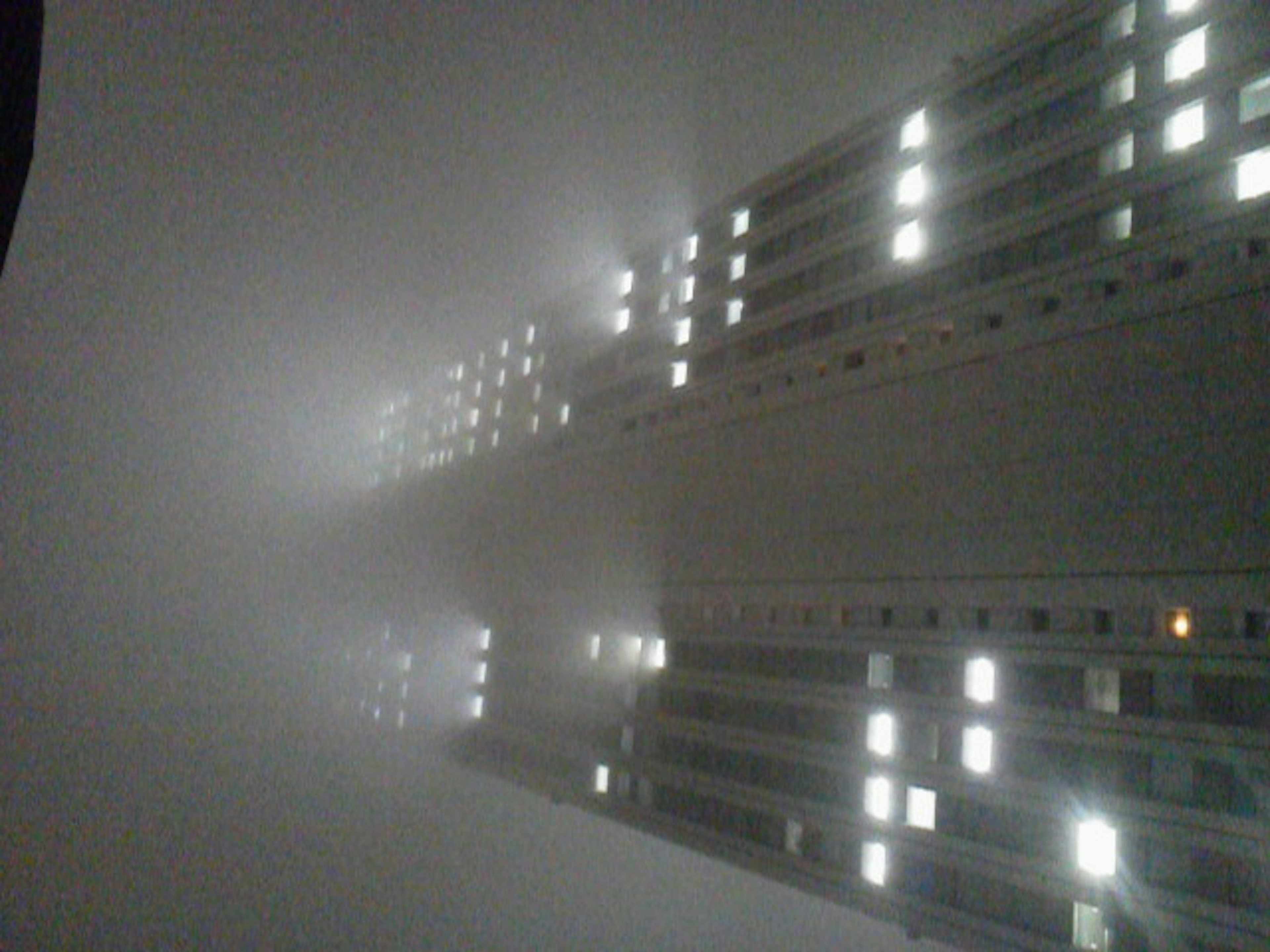 Tall building shrouded in fog with lights glowing from windows