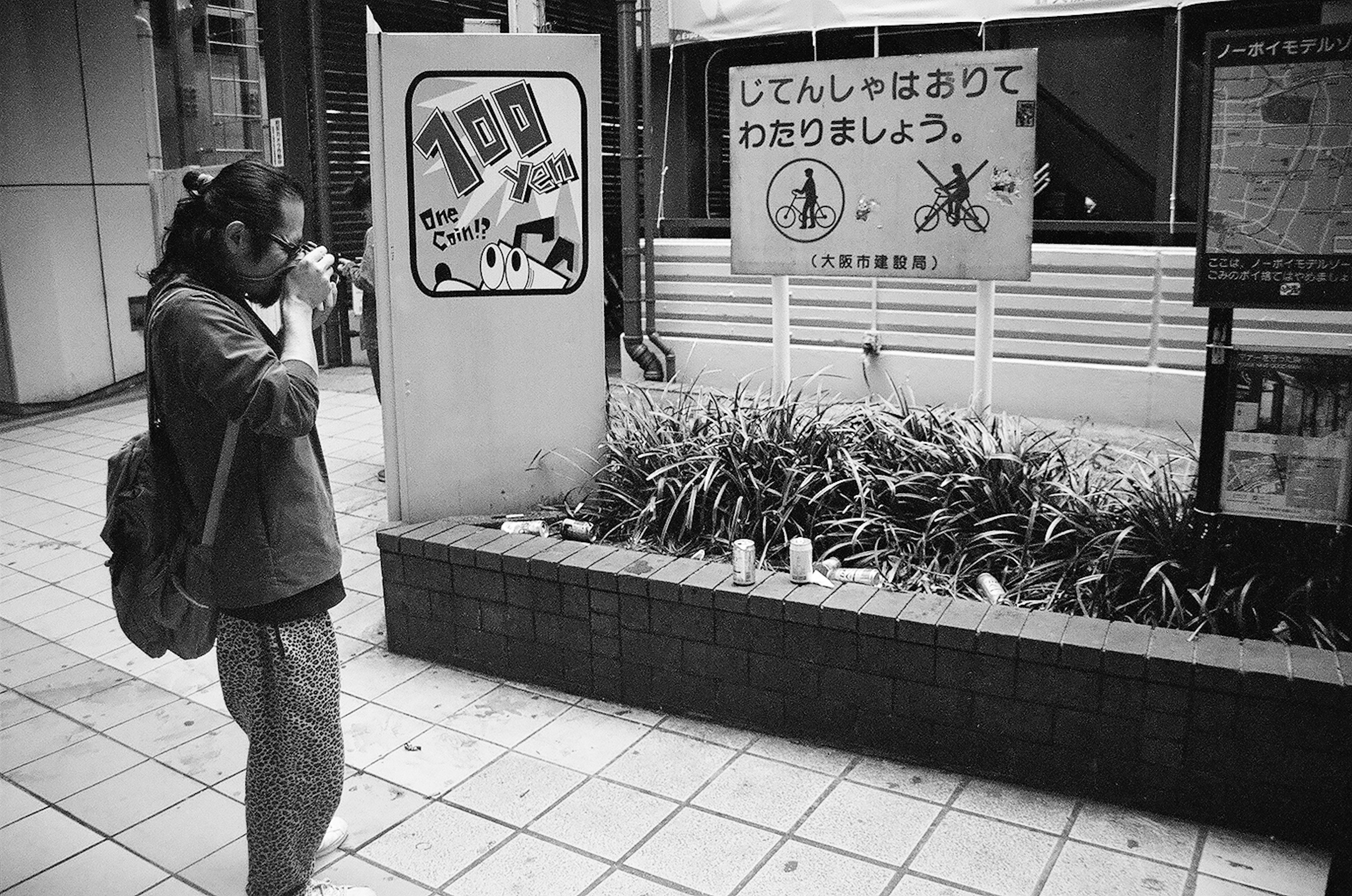 モノクロの街角でカメラを構える人物と看板がある風景