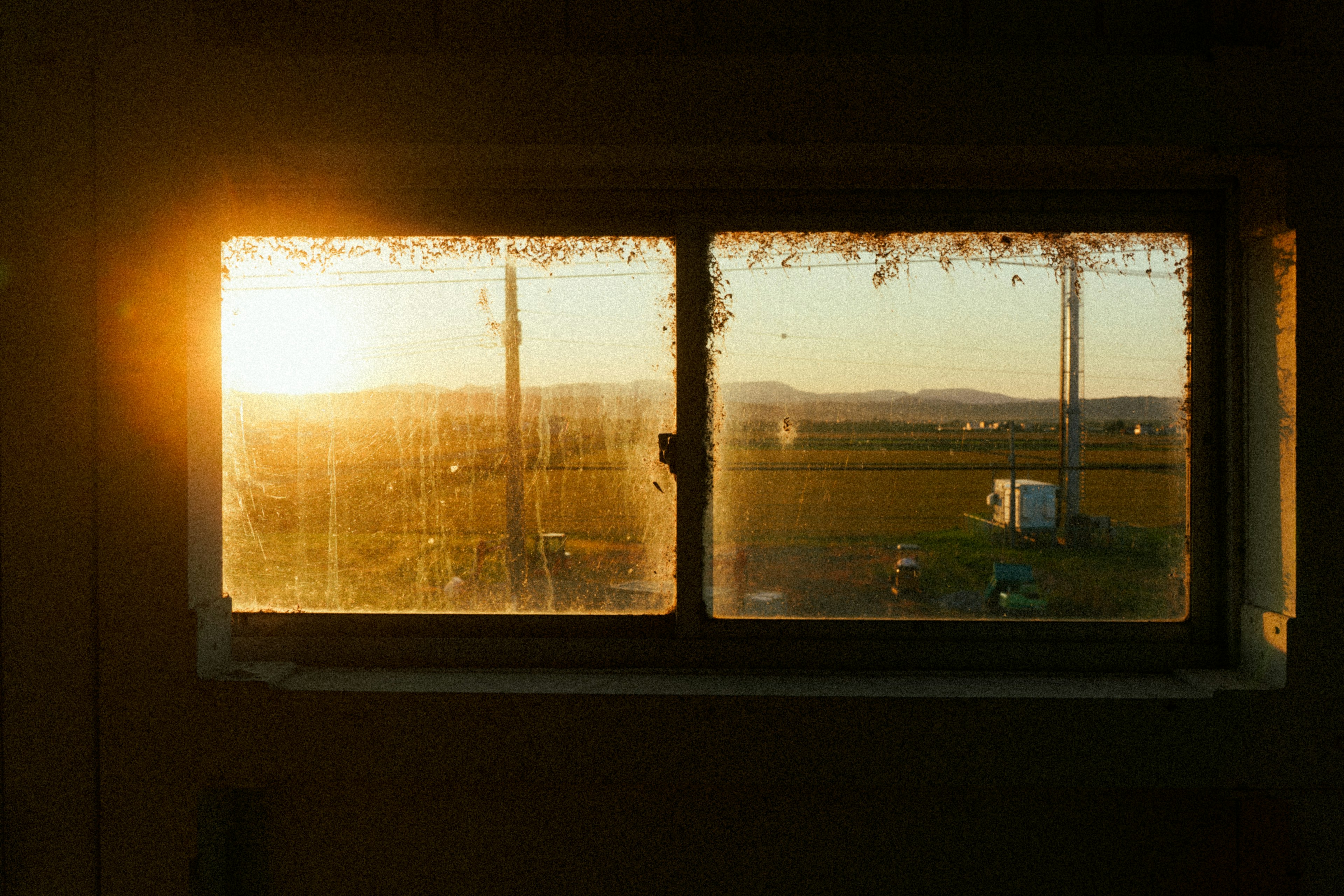 View of sunrise through a window with a rural landscape and distant mountains