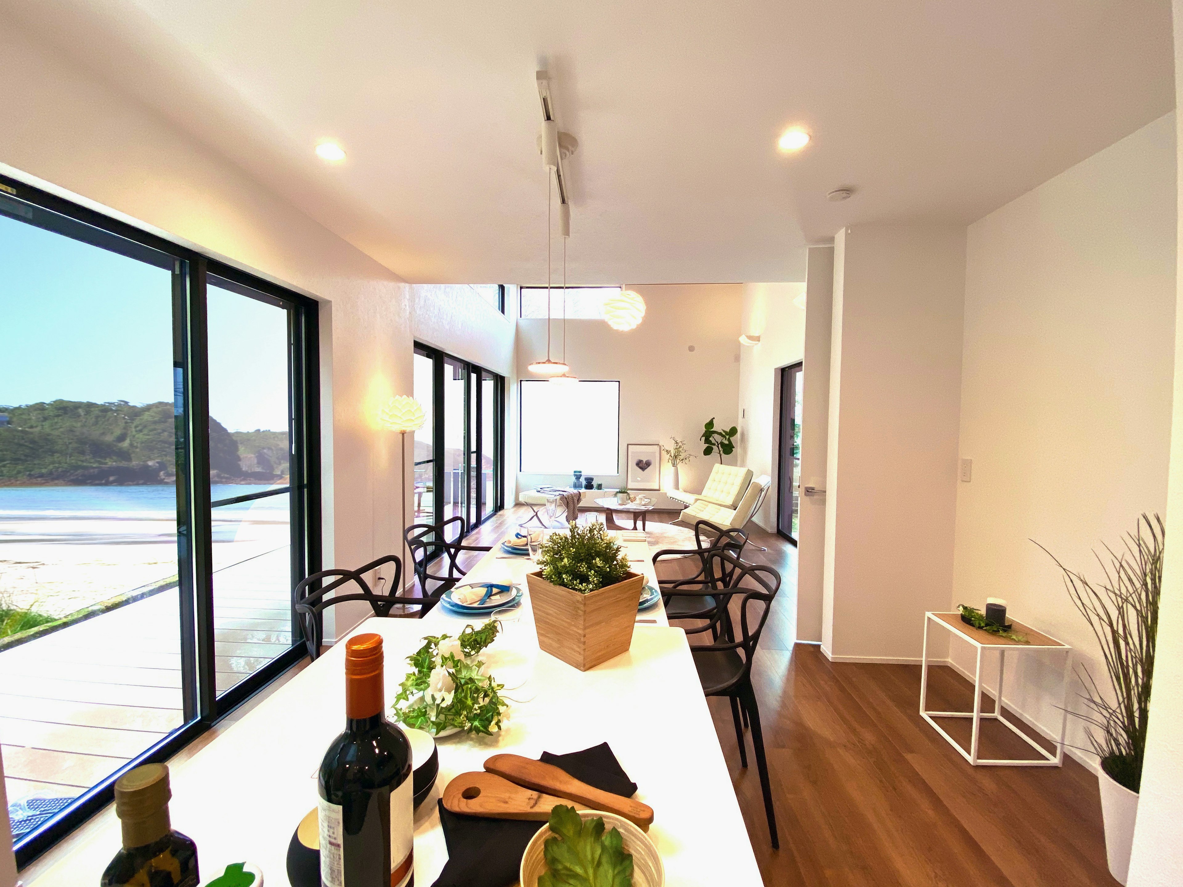 Modern dining space view with natural light from windows featuring plants and wine bottles on the table