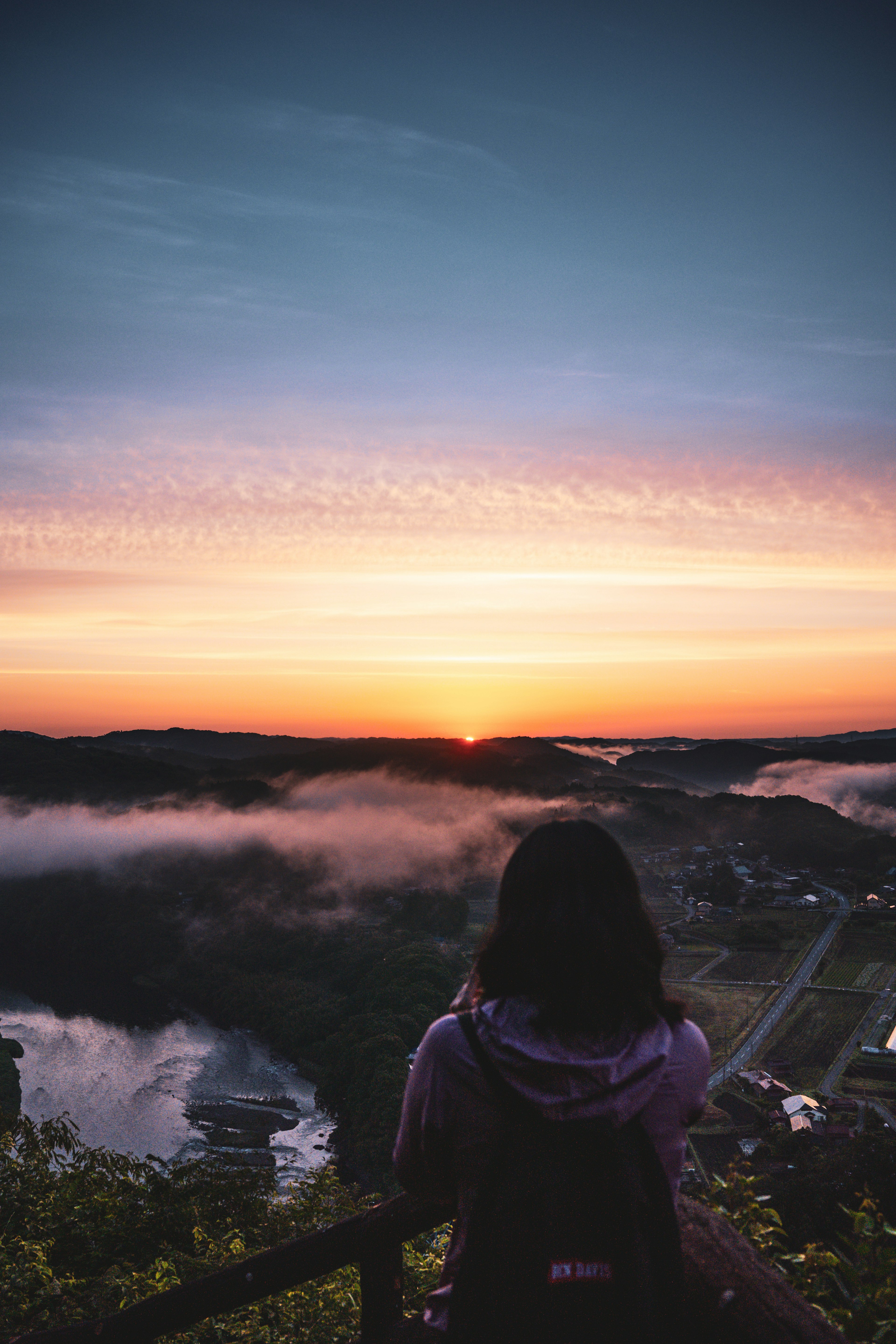 Femme surplombant une vallée au coucher du soleil avec de la brume et des nuages