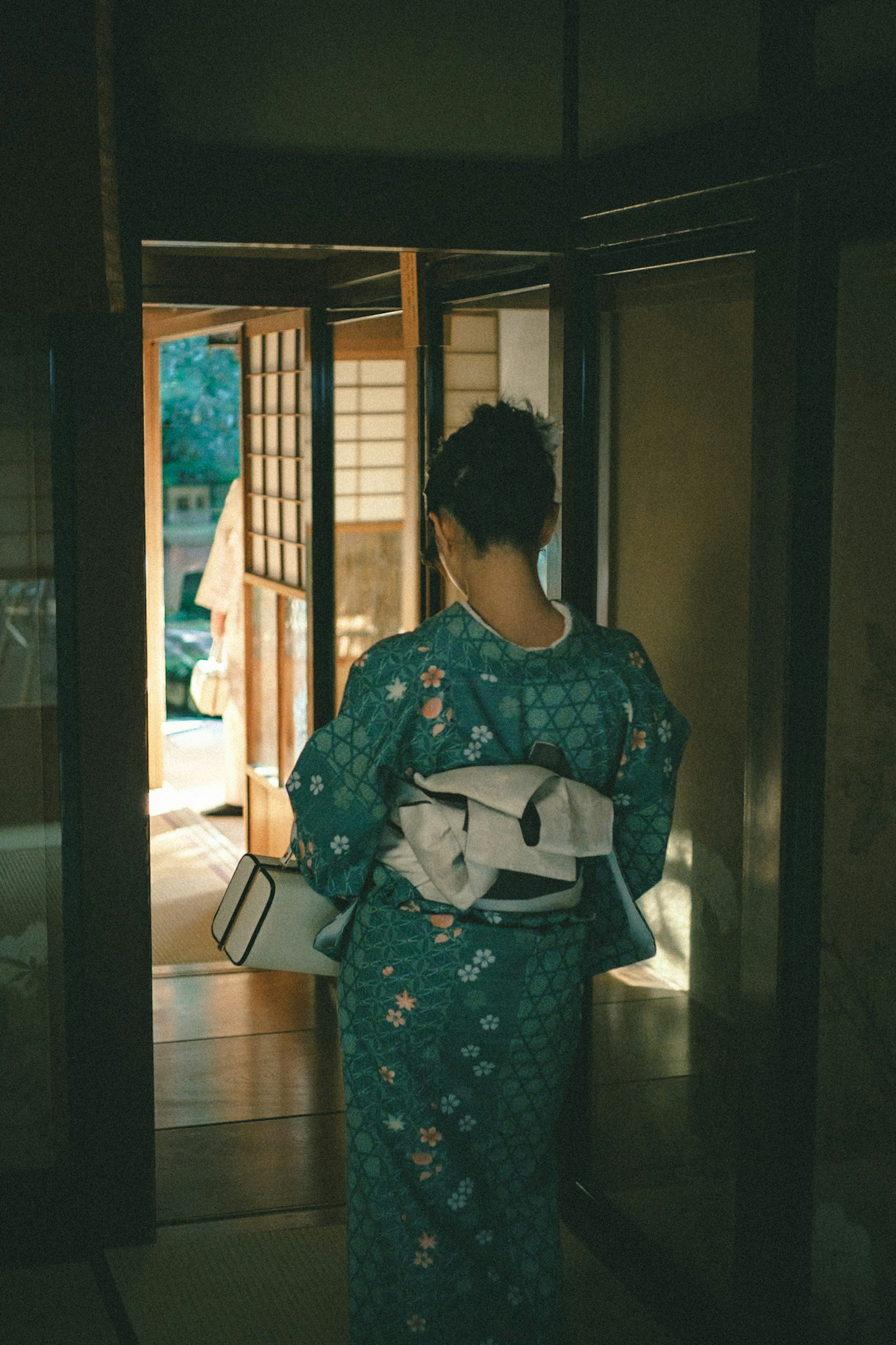 Seorang wanita dalam kimono biru berdiri membelakangi kamera di sebuah ruangan