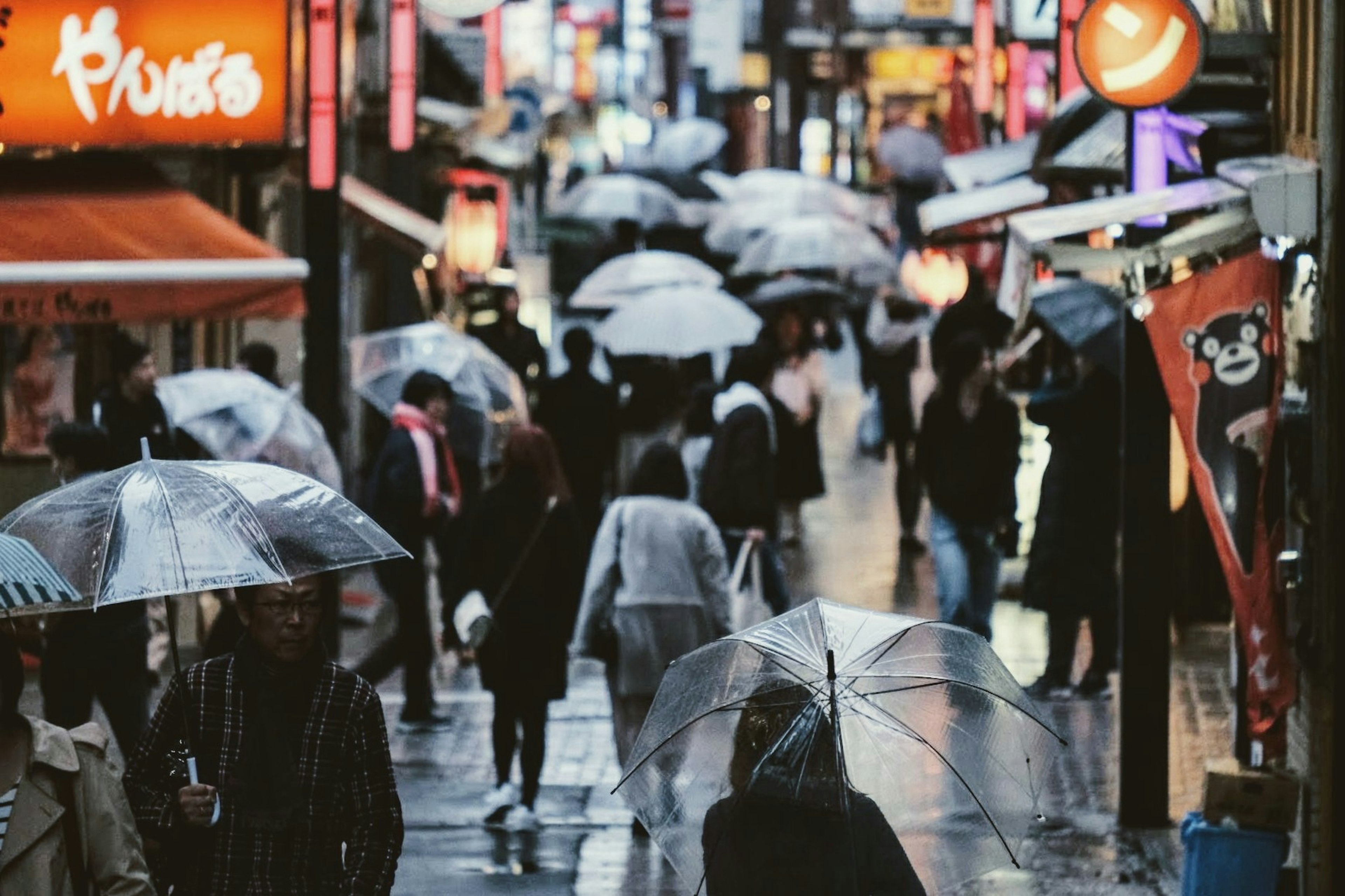 雨の中、透明な傘を持った人々が歩く賑やかな通りの風景