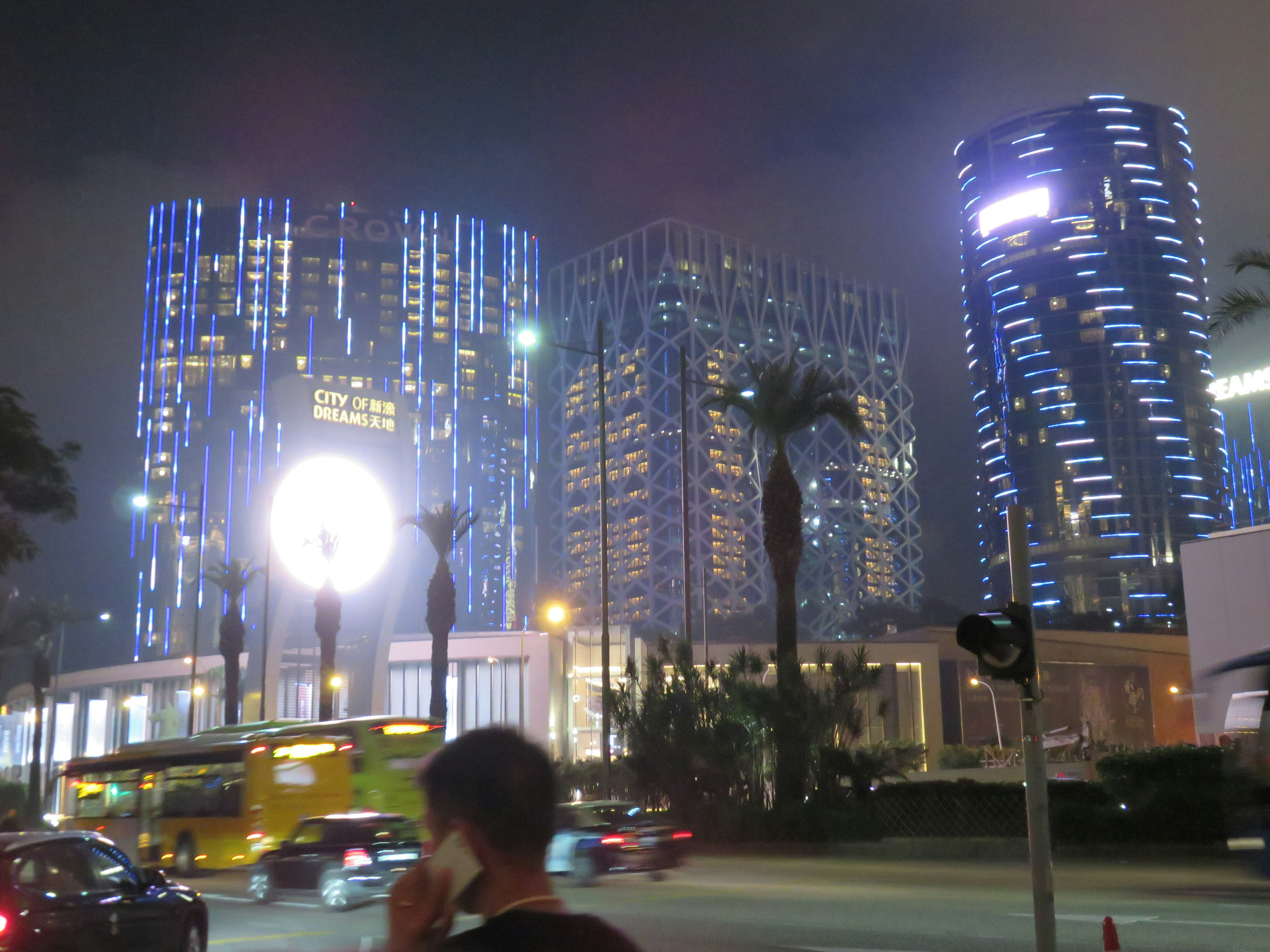 Night cityscape with skyscrapers illuminated in blue lights featuring cars and pedestrians