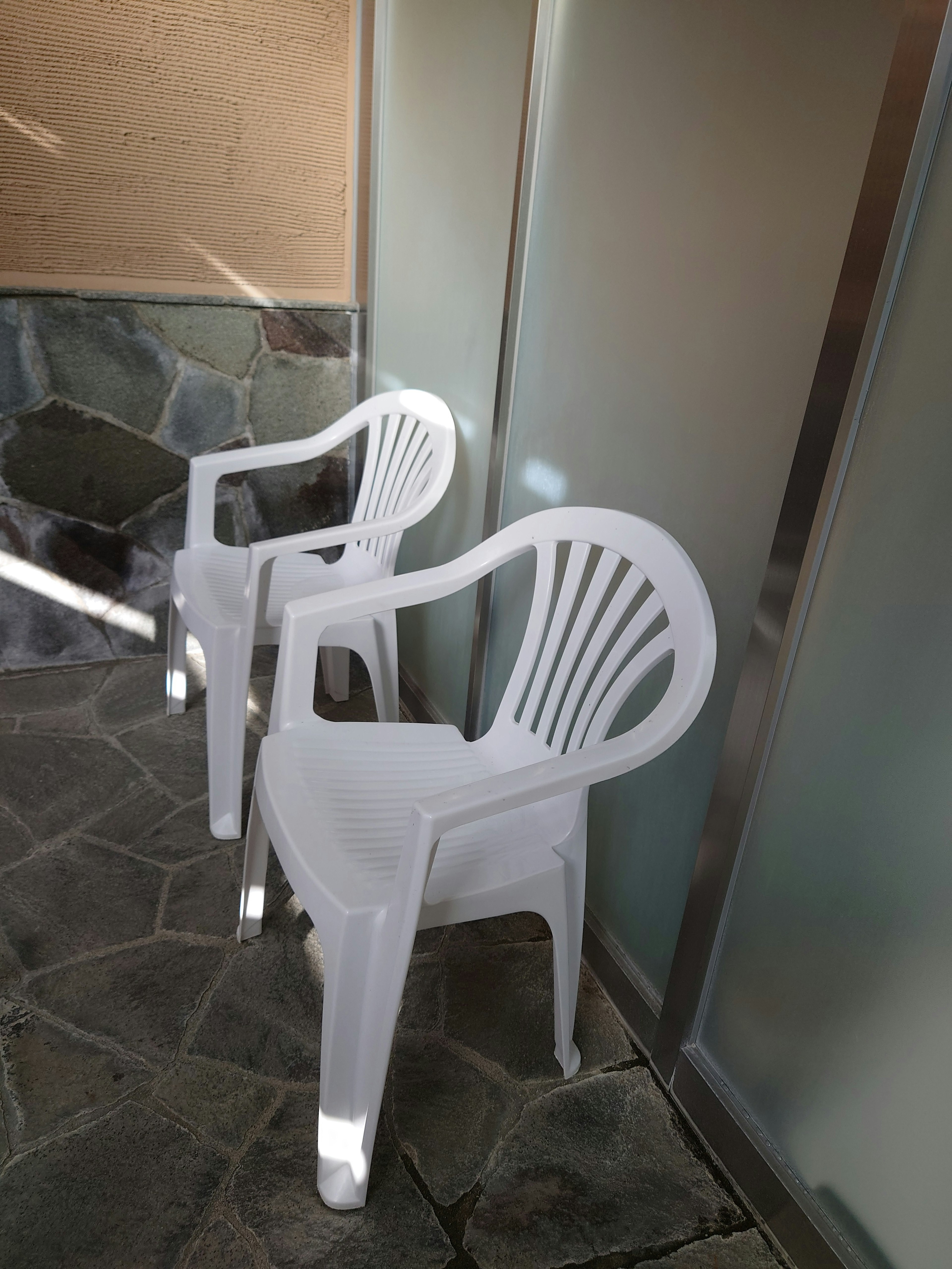 Two white plastic chairs placed next to a glass wall