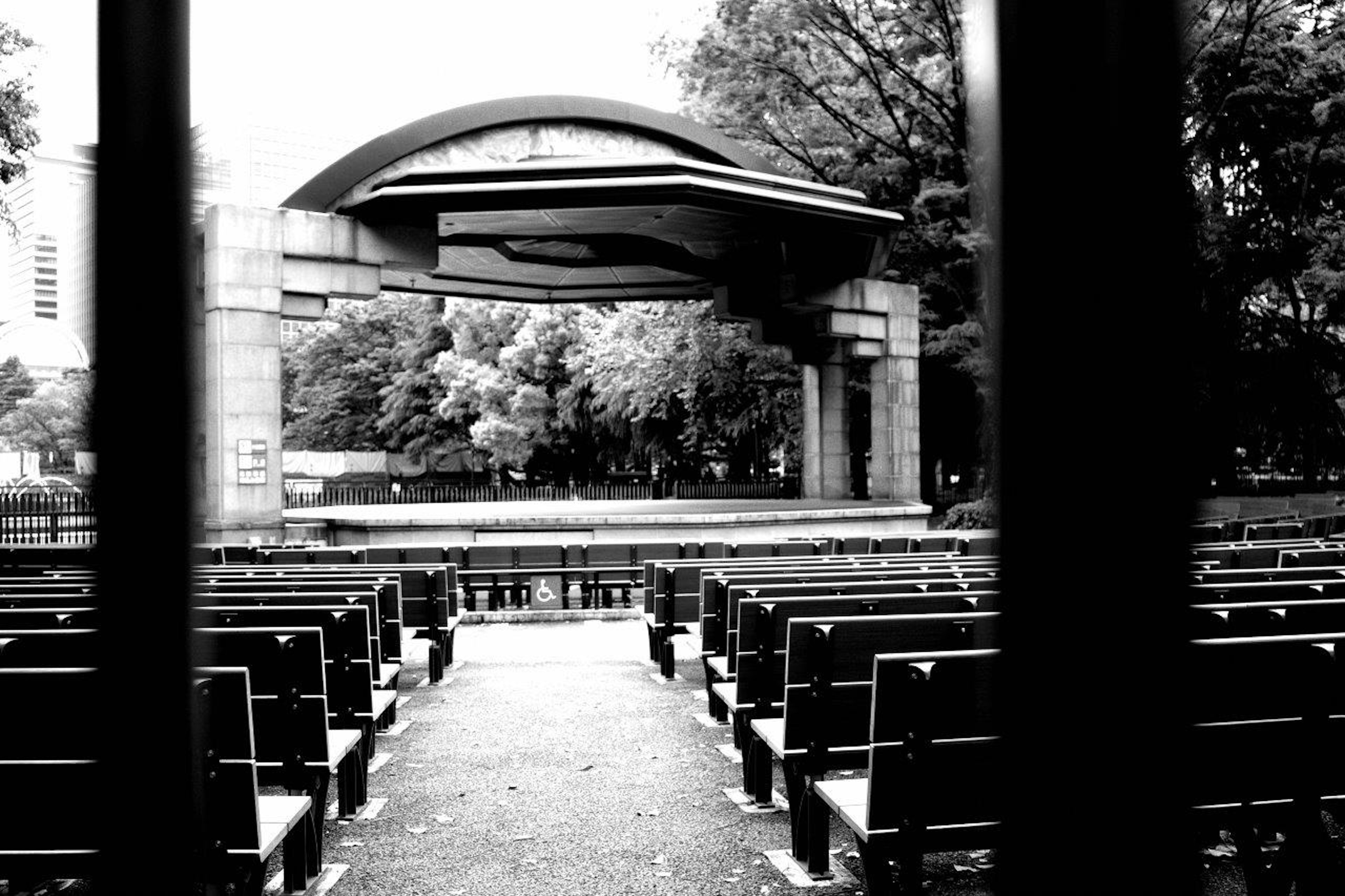 Black and white photo of an outdoor stage in a park with empty benches