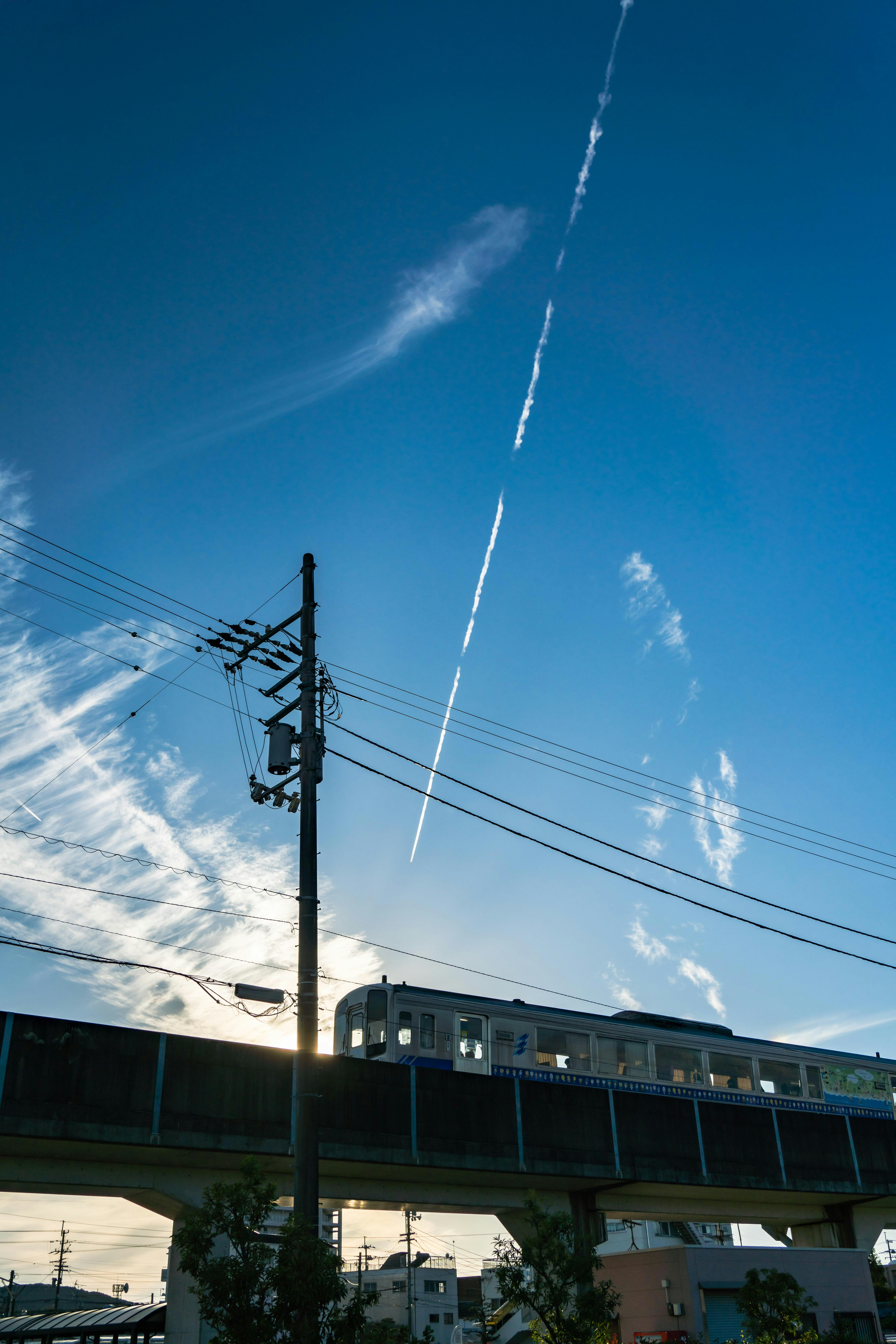 Silhouette di un treno che corre sotto un cielo blu con linee elettriche e nuvole sottili