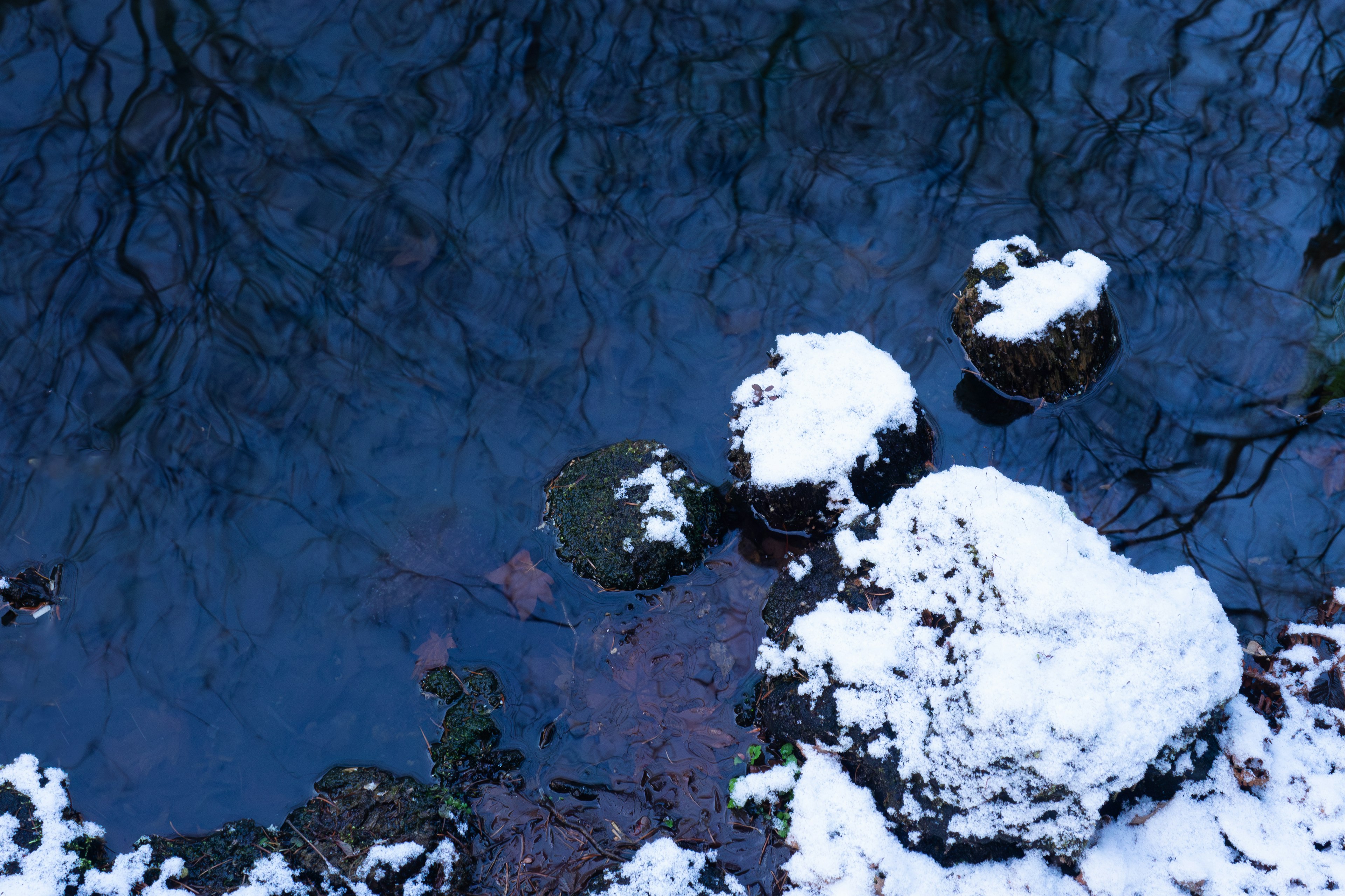 雪をかぶった石と青い水面のコントラストが美しい小川の風景