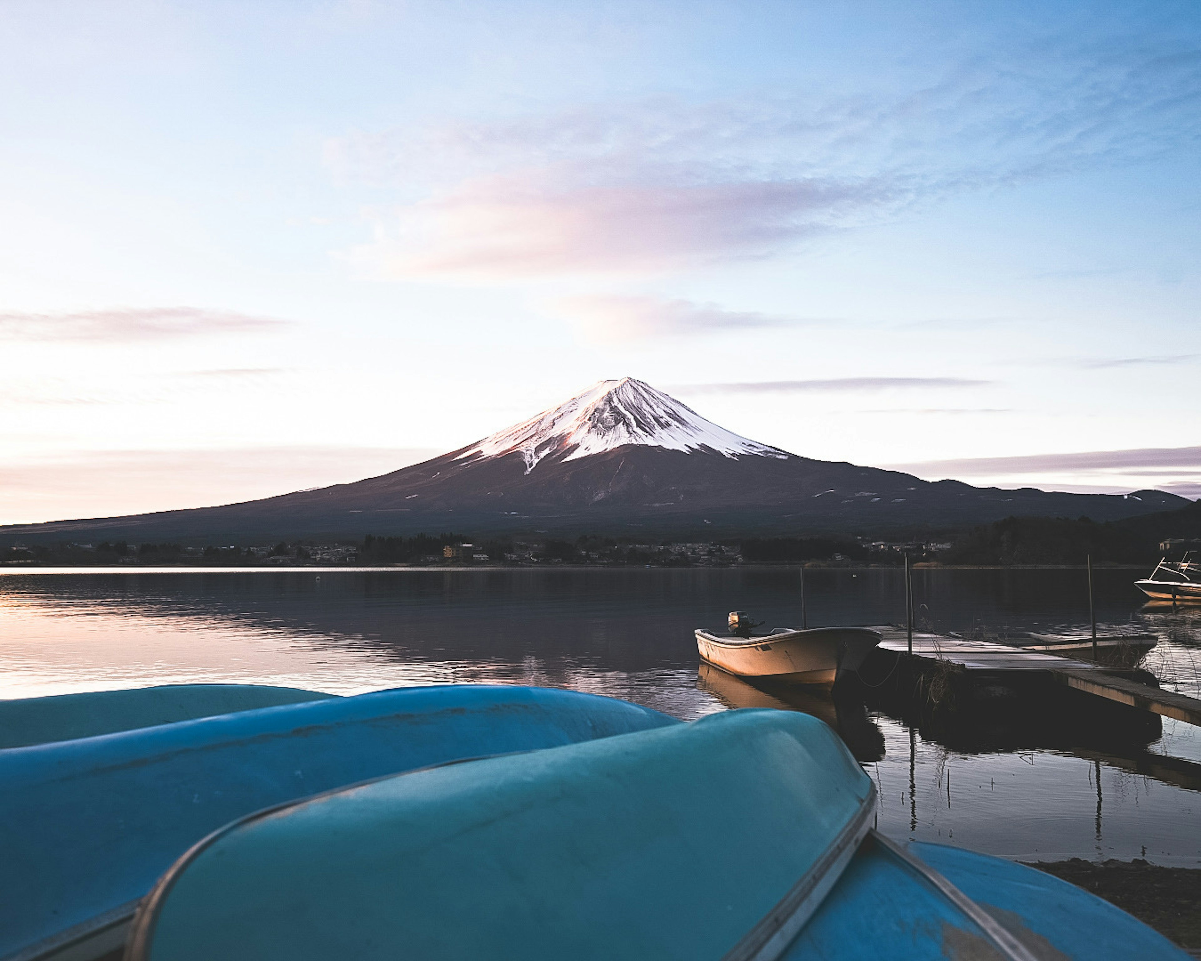 ทิวทัศน์ที่สวยงามของภูเขาฟูจิพร้อมทะเลสาบสงบเรือสีน้ำเงินในพื้นหลังและท้องฟ้าตอนรุ่ง