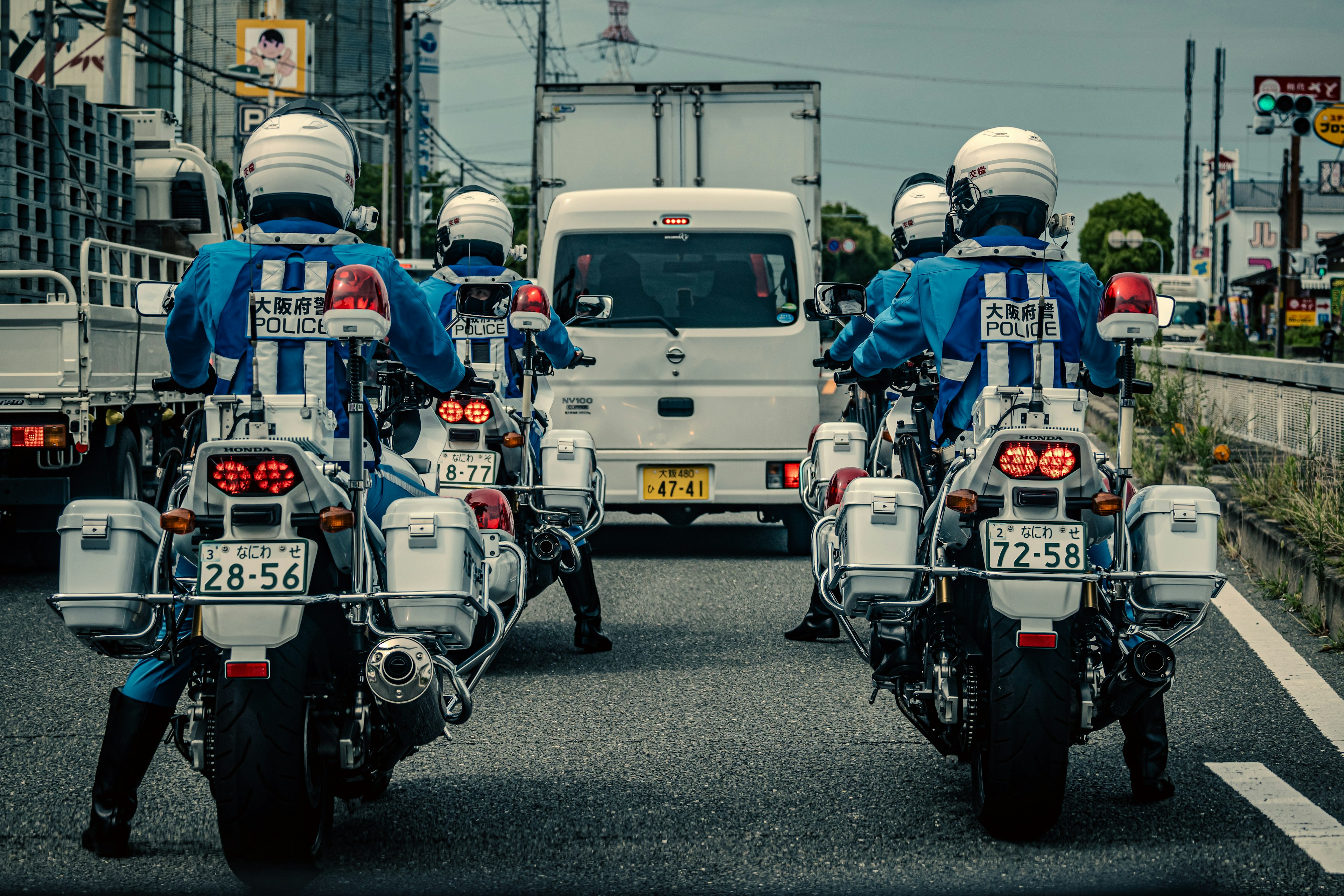 A police motorcycle squad in blue uniforms lined up behind a white vehicle