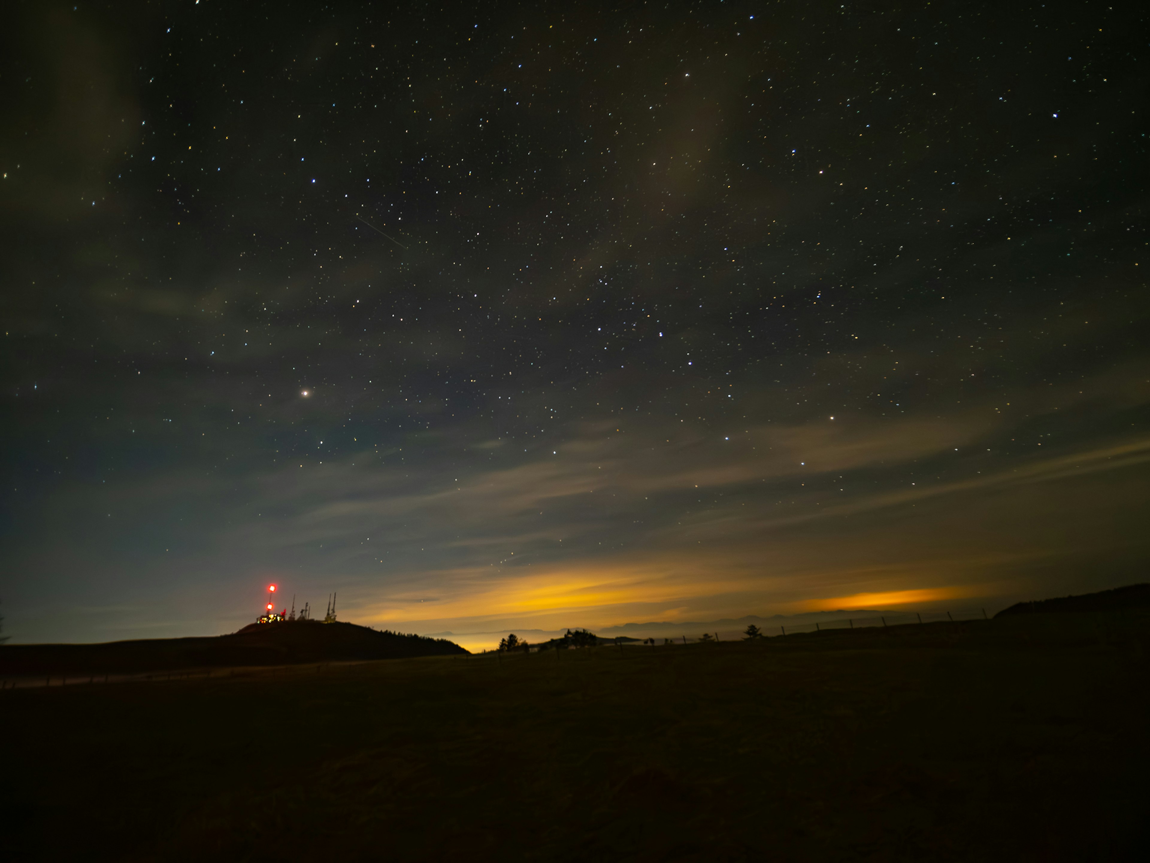 Paisaje nocturno con un cielo estrellado y nubes con una torre roja en el horizonte bajo