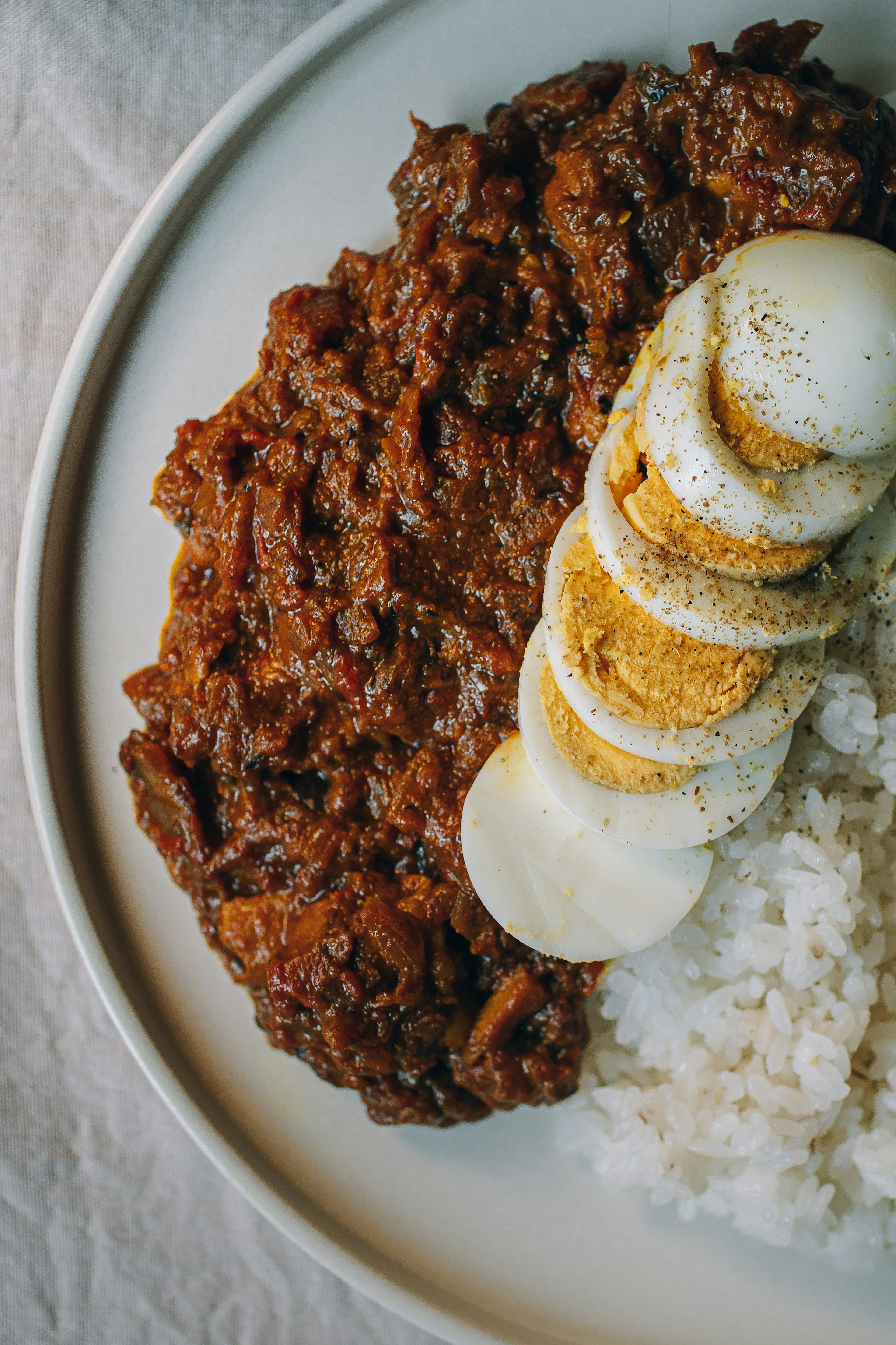 Sepiring nasi disajikan dengan telur rebus yang diiris dan hidangan daging