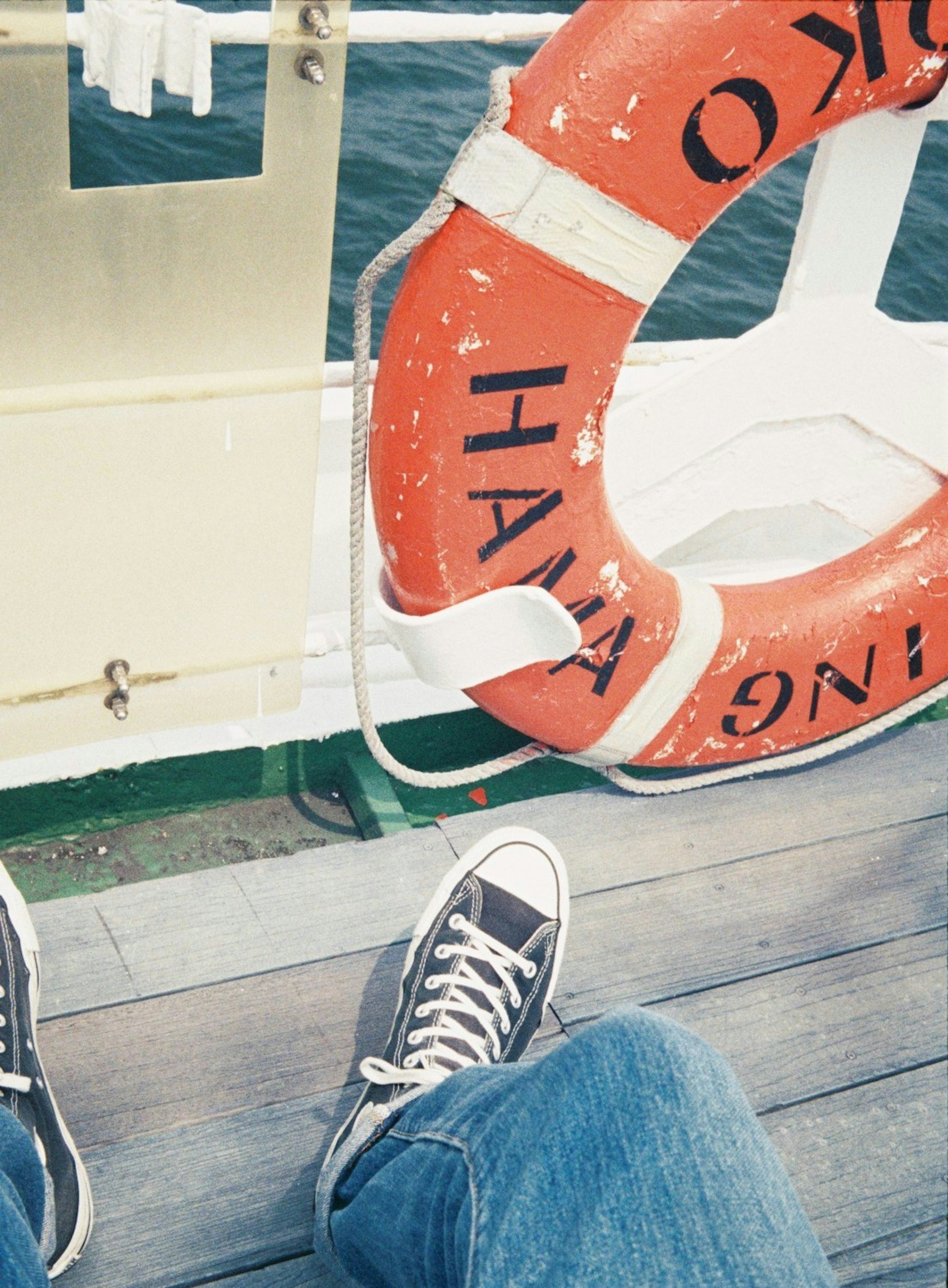 Foto von Füßen in Turnschuhen neben einem Rettungsring auf dem Deck eines Bootes