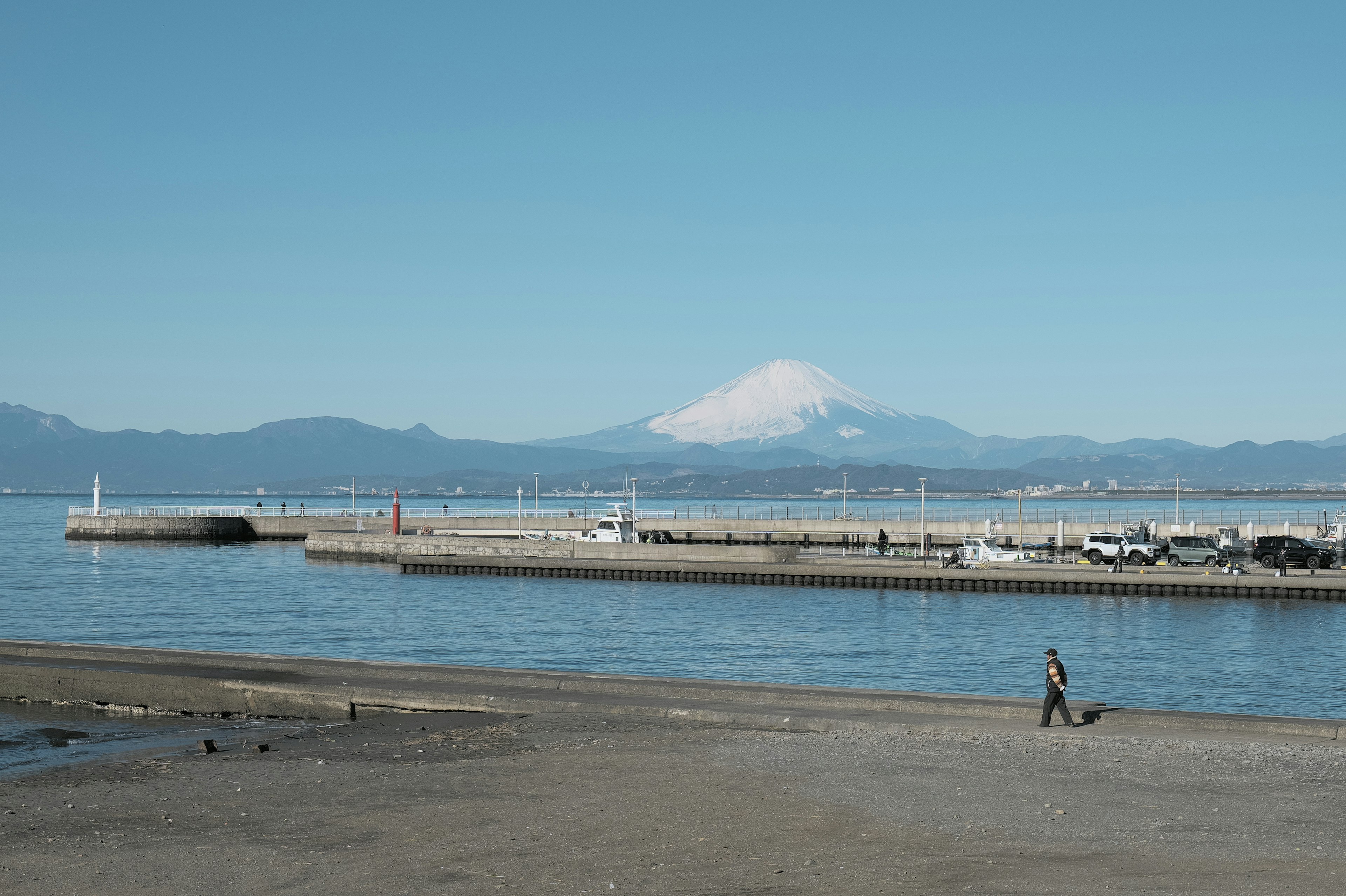 Eine Person, die am Strand mit Blick auf das ruhige Meer und die Berge spaziert