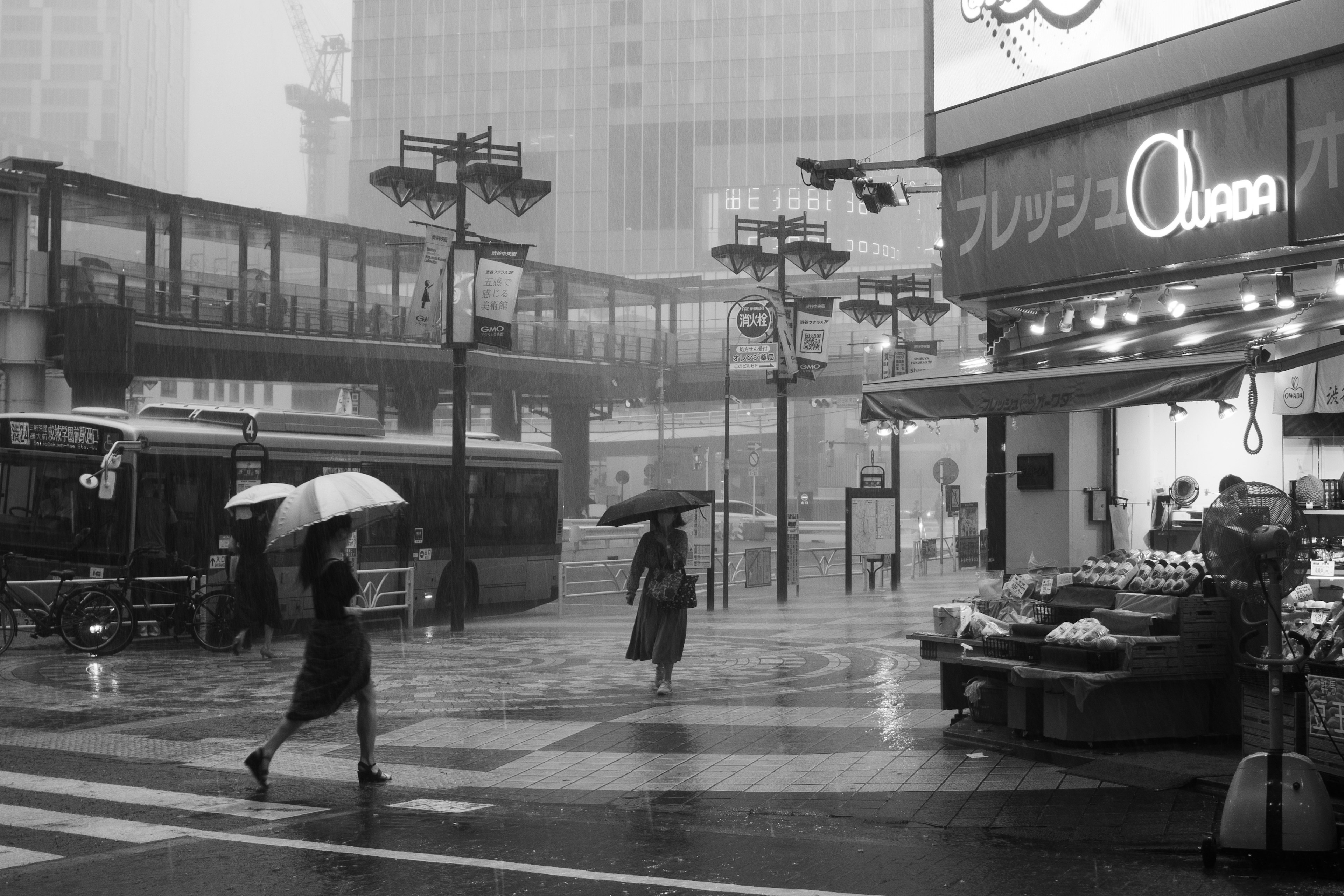 Personas caminando bajo la lluvia con paraguas cerca de un mercado