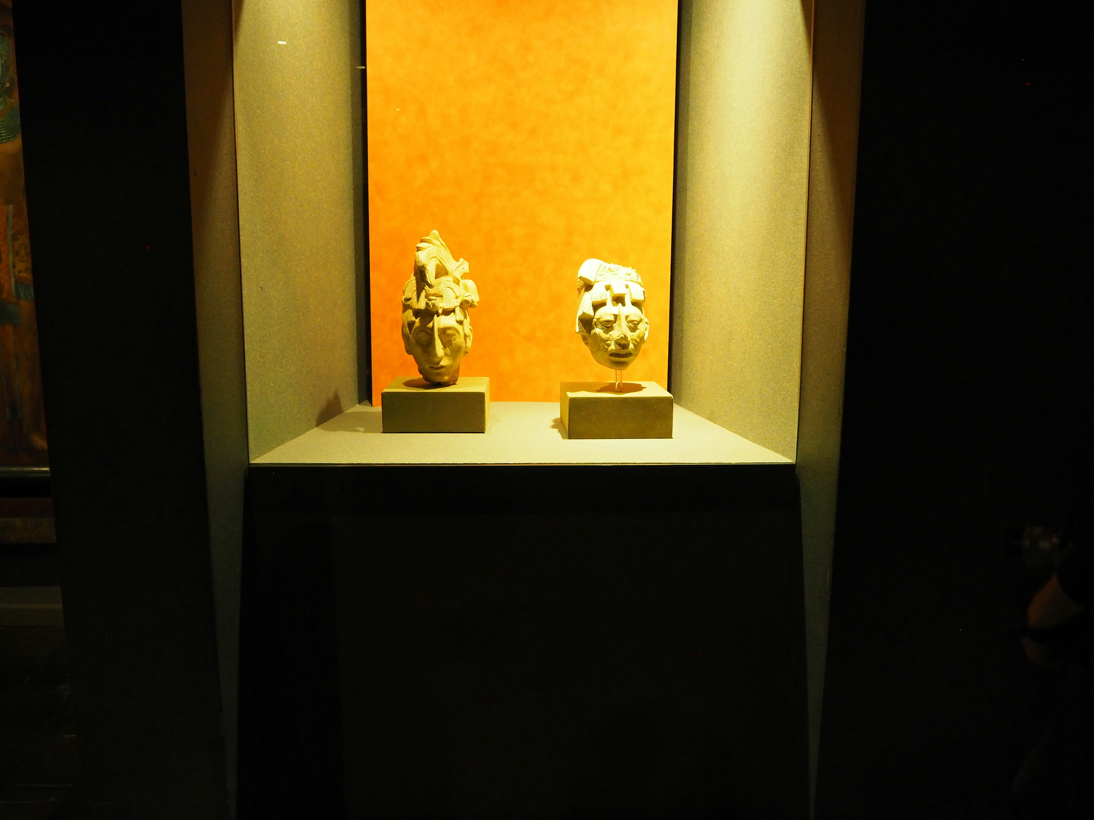 Image de deux sculptures exposées dans une vitrine avec un fond orange