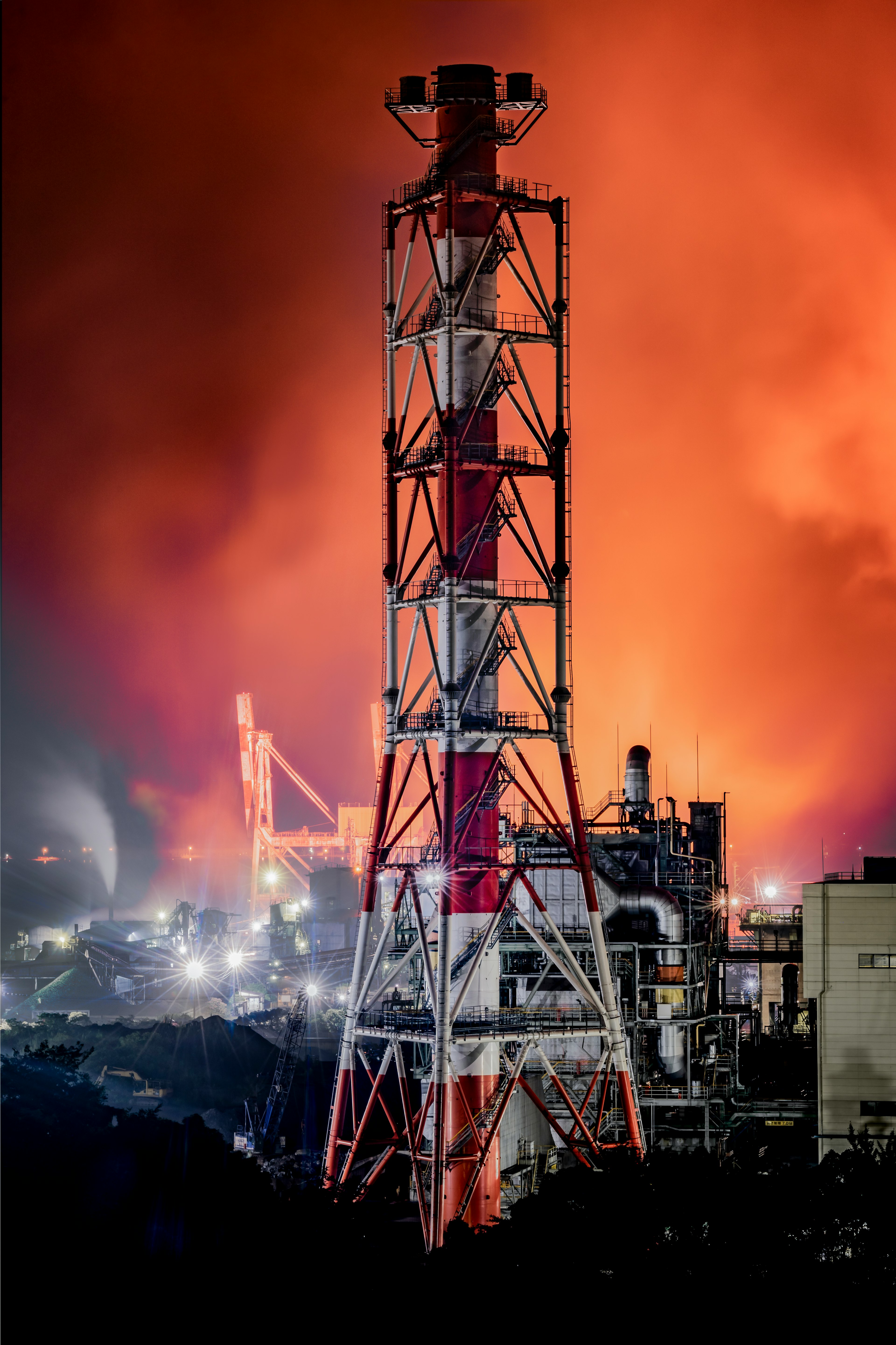 Rote und weiße Schornsteine vor einer Industrieansicht mit orangefarbenem Himmel