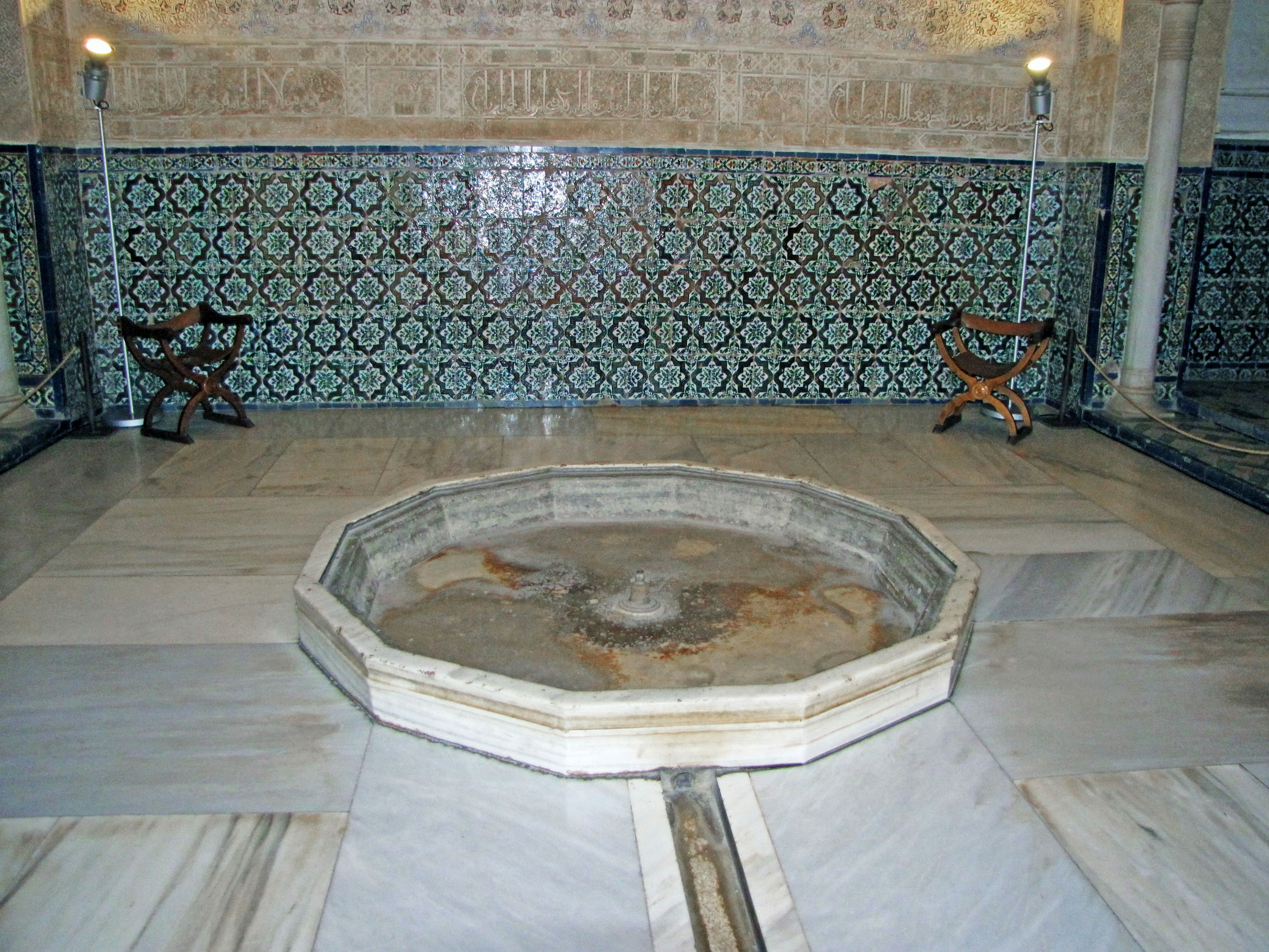 Interior of a hamam featuring an octagonal basin with mosaic tile walls and marble flooring