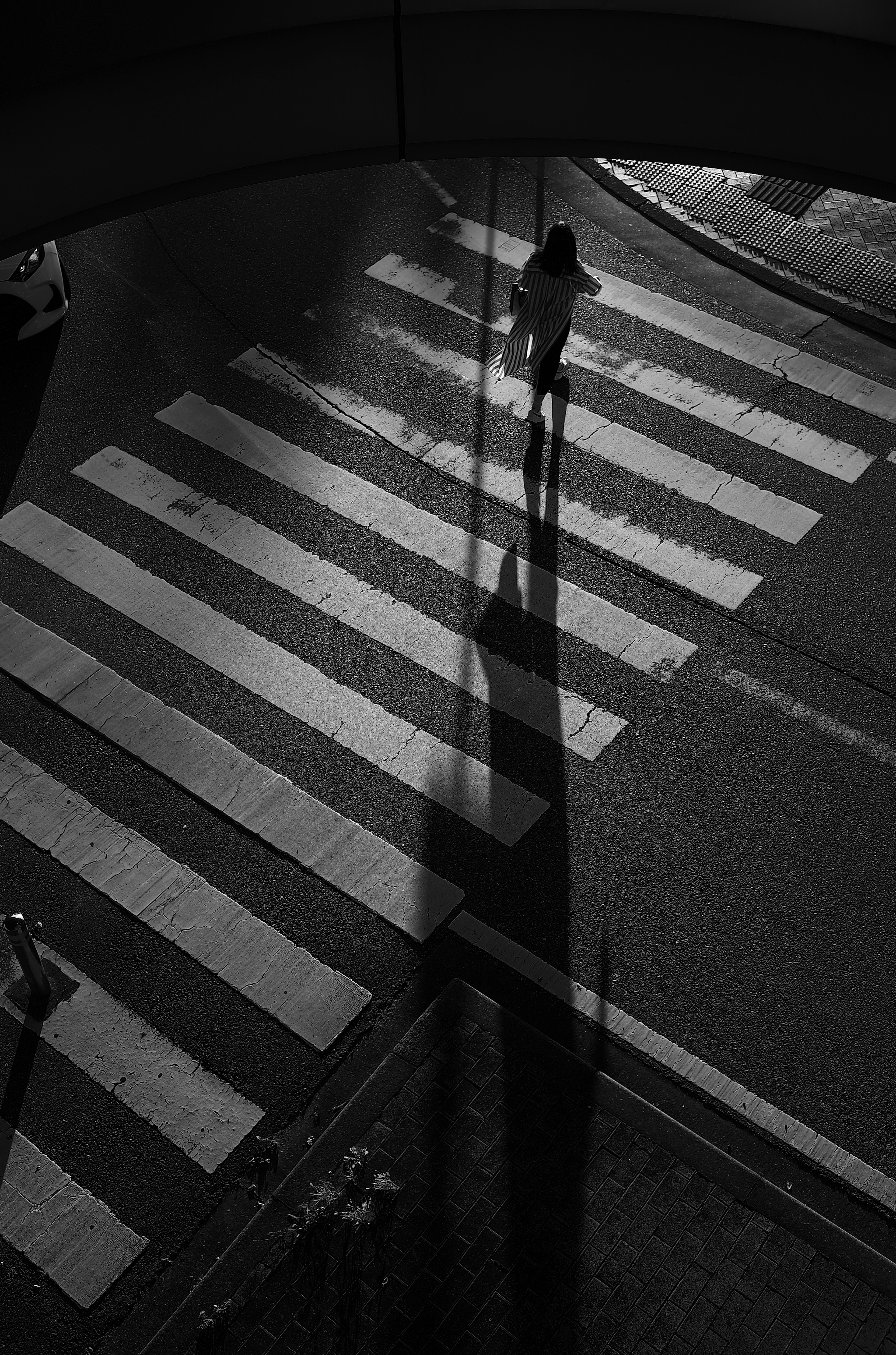 A person's shadow cast long as they walk across a black and white crosswalk