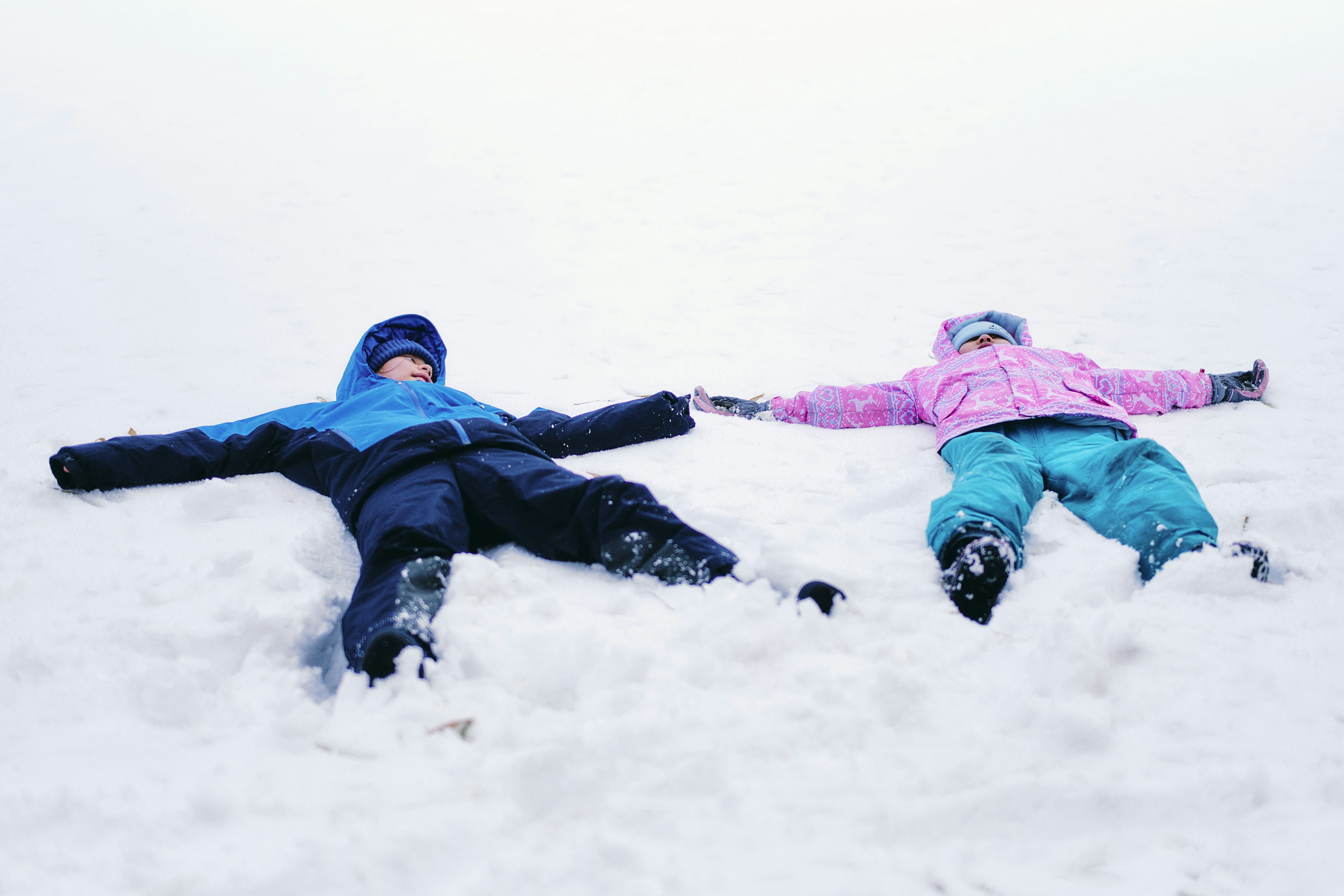 Two children making snow angels in a snowy landscape