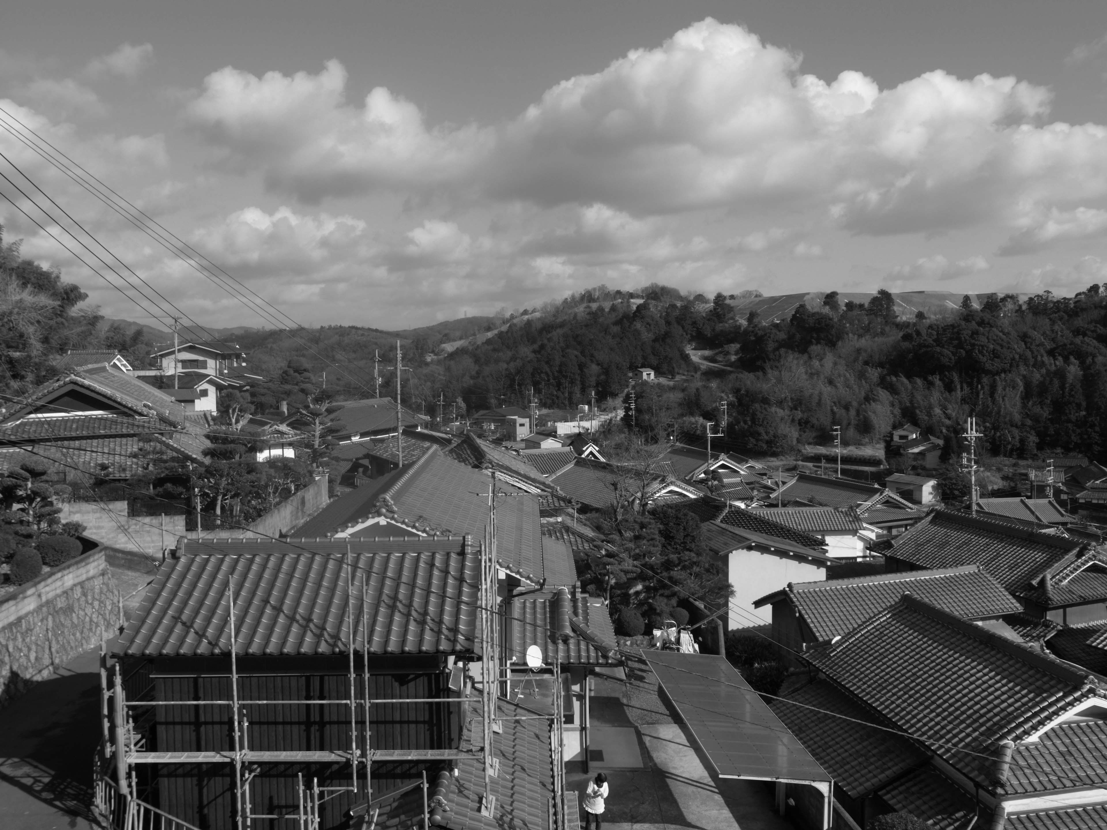 Photo de paysage en noir et blanc montrant la vue d'une ville depuis un toit avec un ciel nuageux et des collines verdoyantes