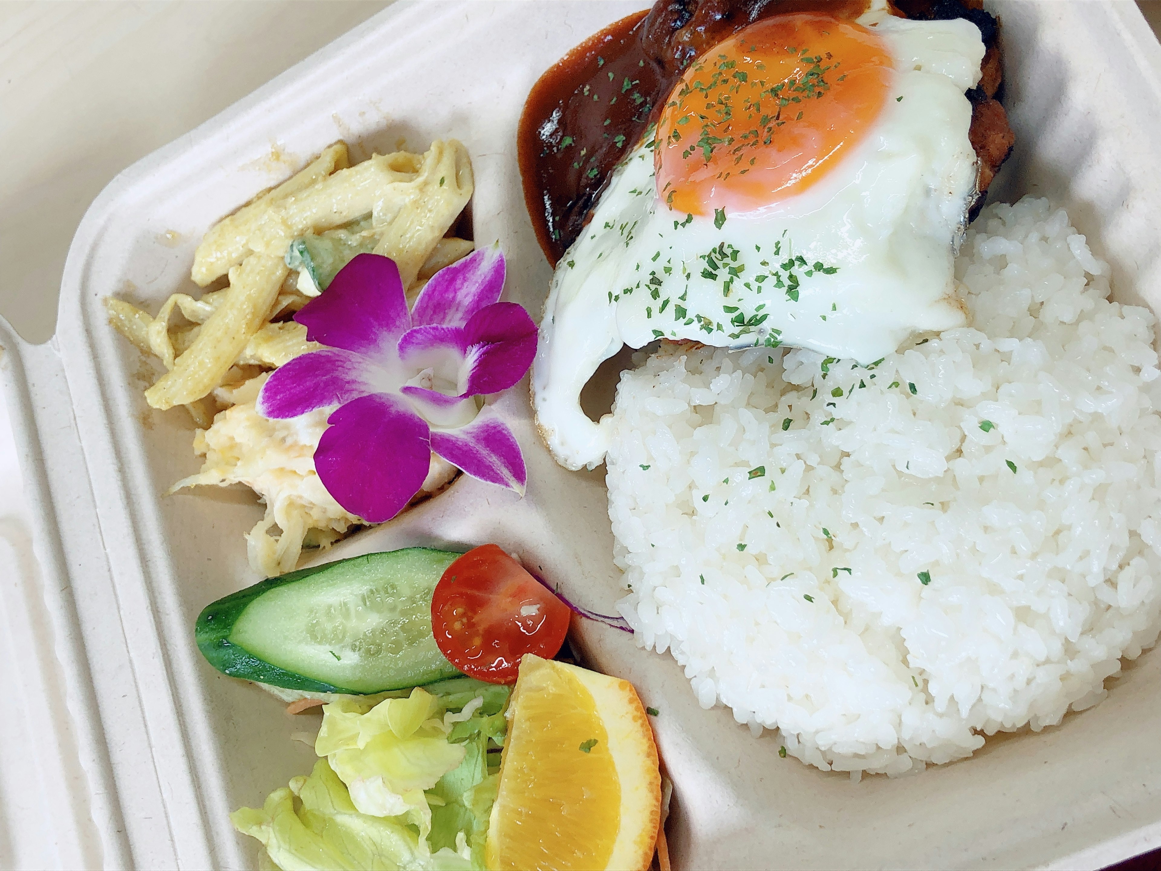 Piring berisi nasi putih dengan telur goreng di atasnya bersama daging panggang dan salad berwarna-warni