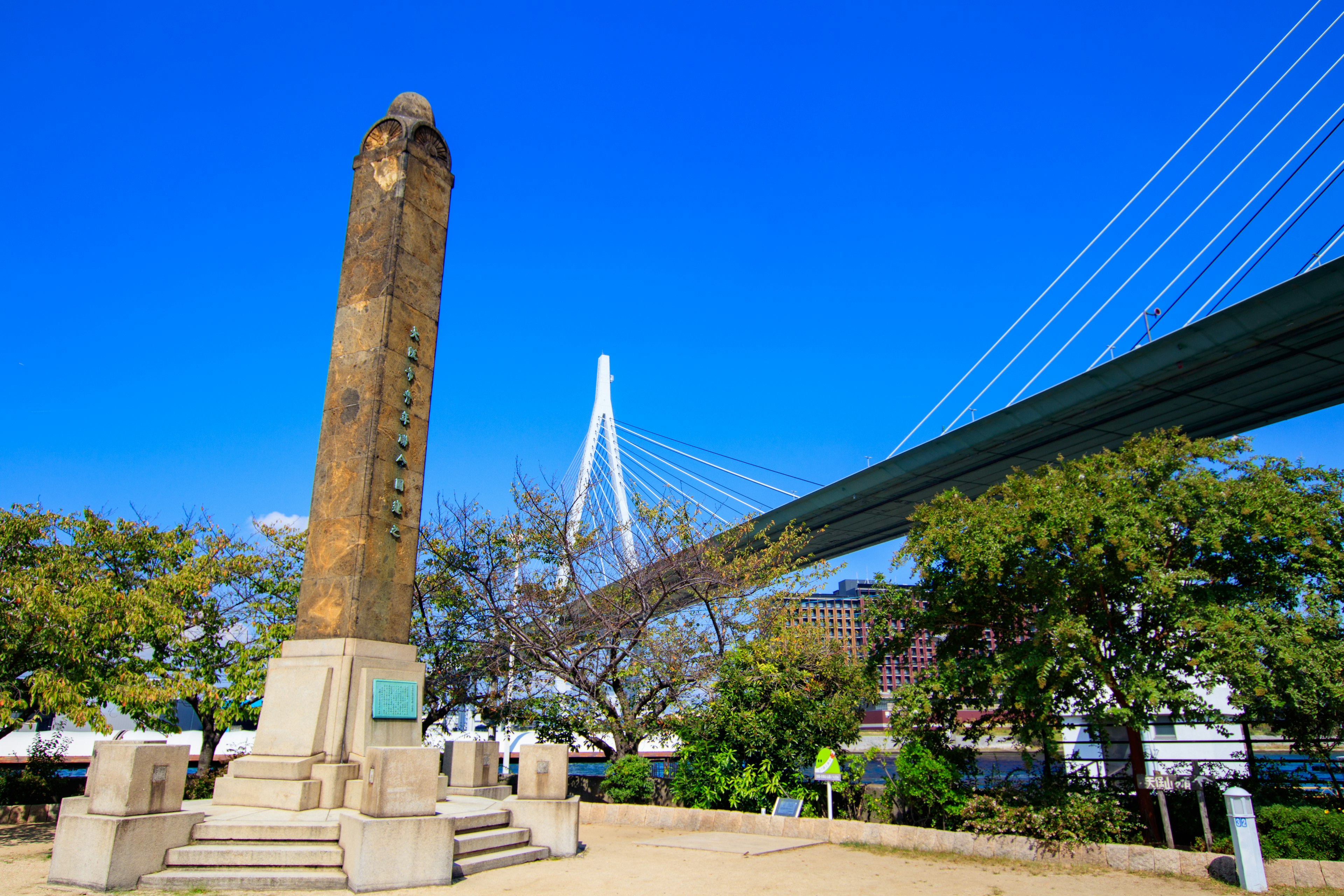 Monumen batu kuno di bawah langit biru cerah dengan jembatan gantung modern di latar belakang