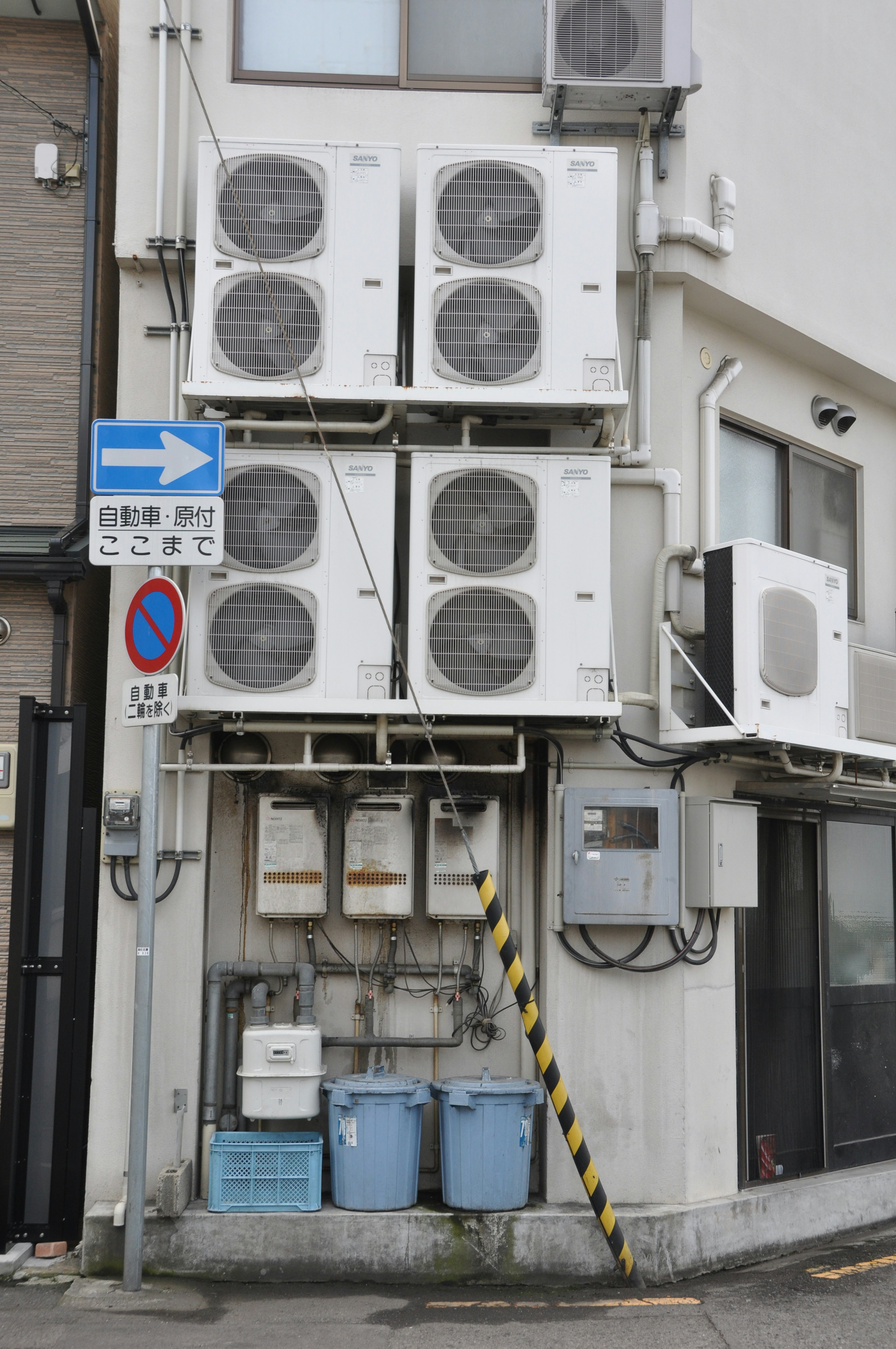 Multiple air conditioning units mounted on a white wall with utility meters