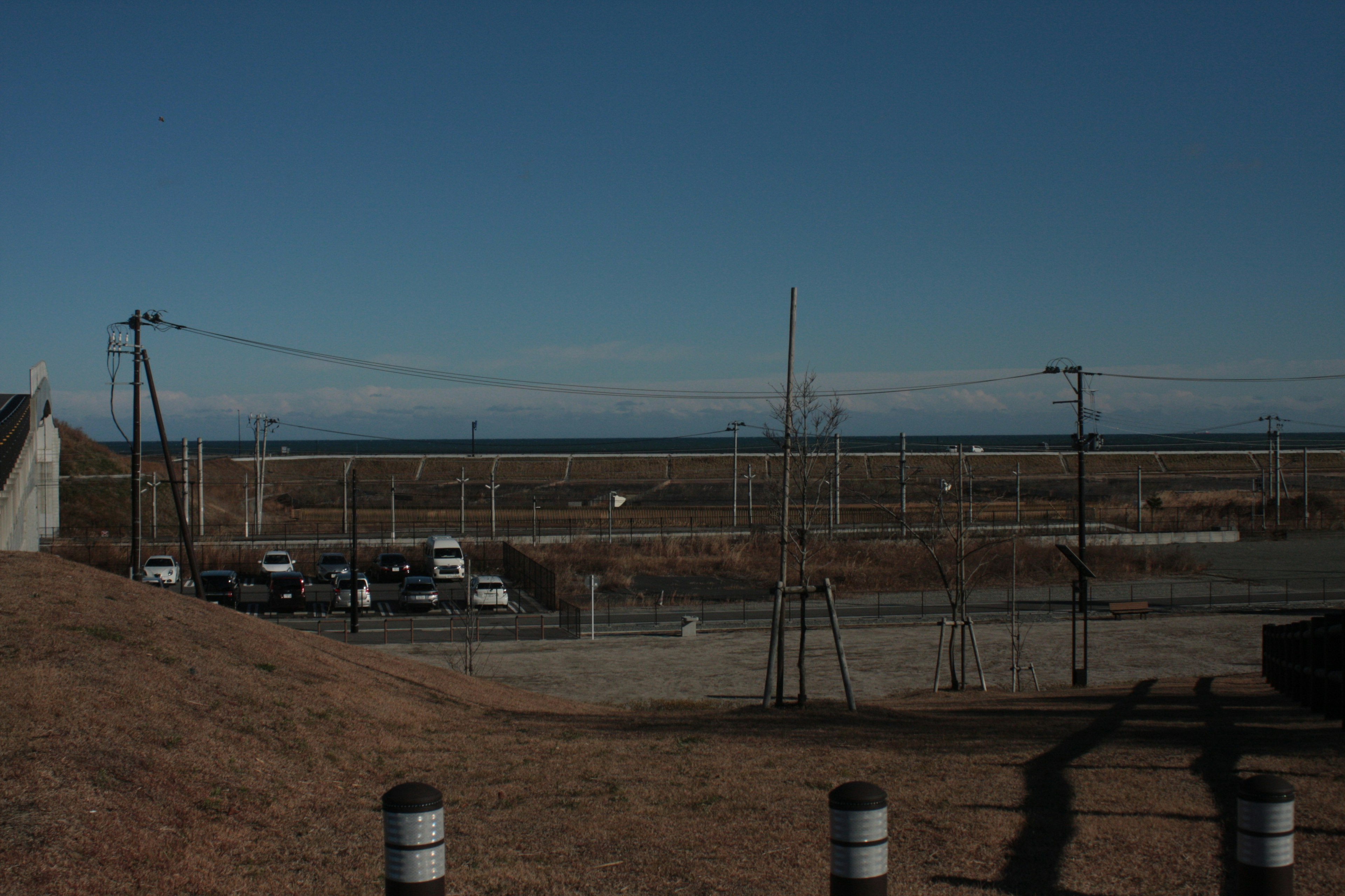 Landscape featuring a blue sky and vast grassland with a parking lot containing several cars and power poles