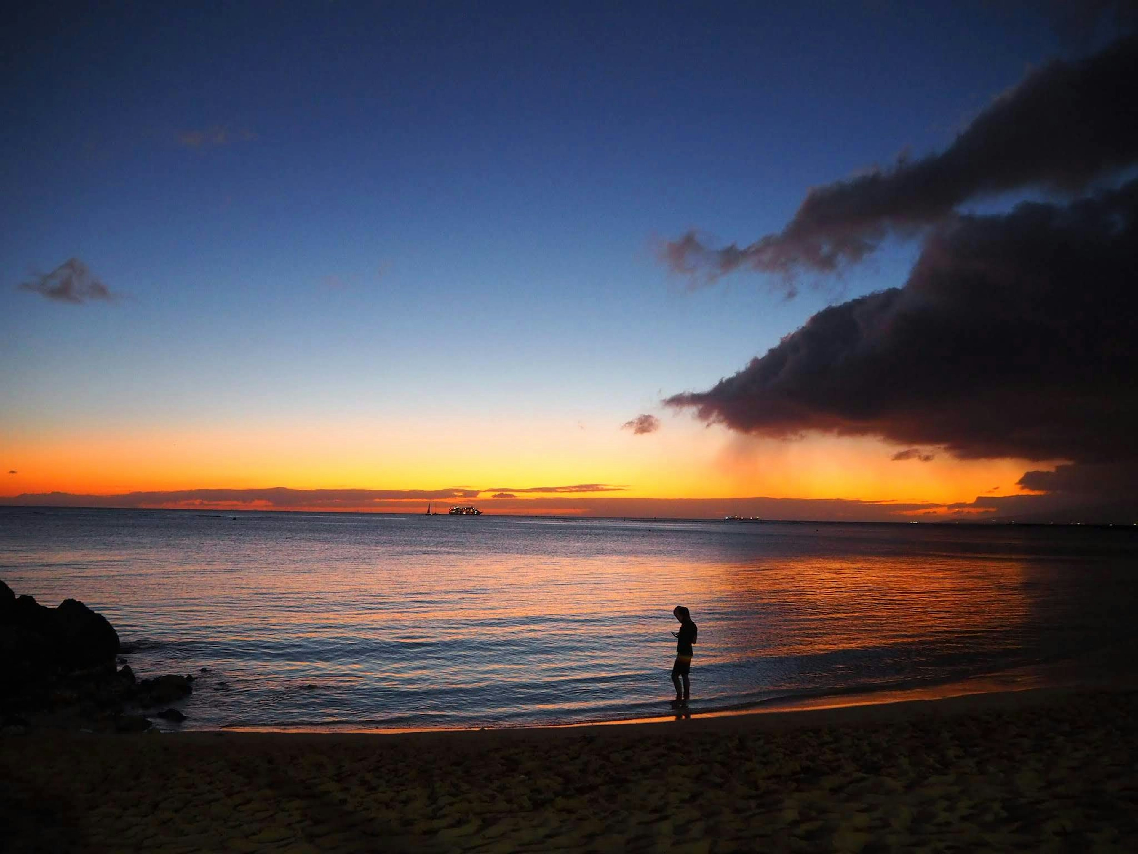 Person steht am Strand während des Sonnenuntergangs mit lebhaften Himmelstönen