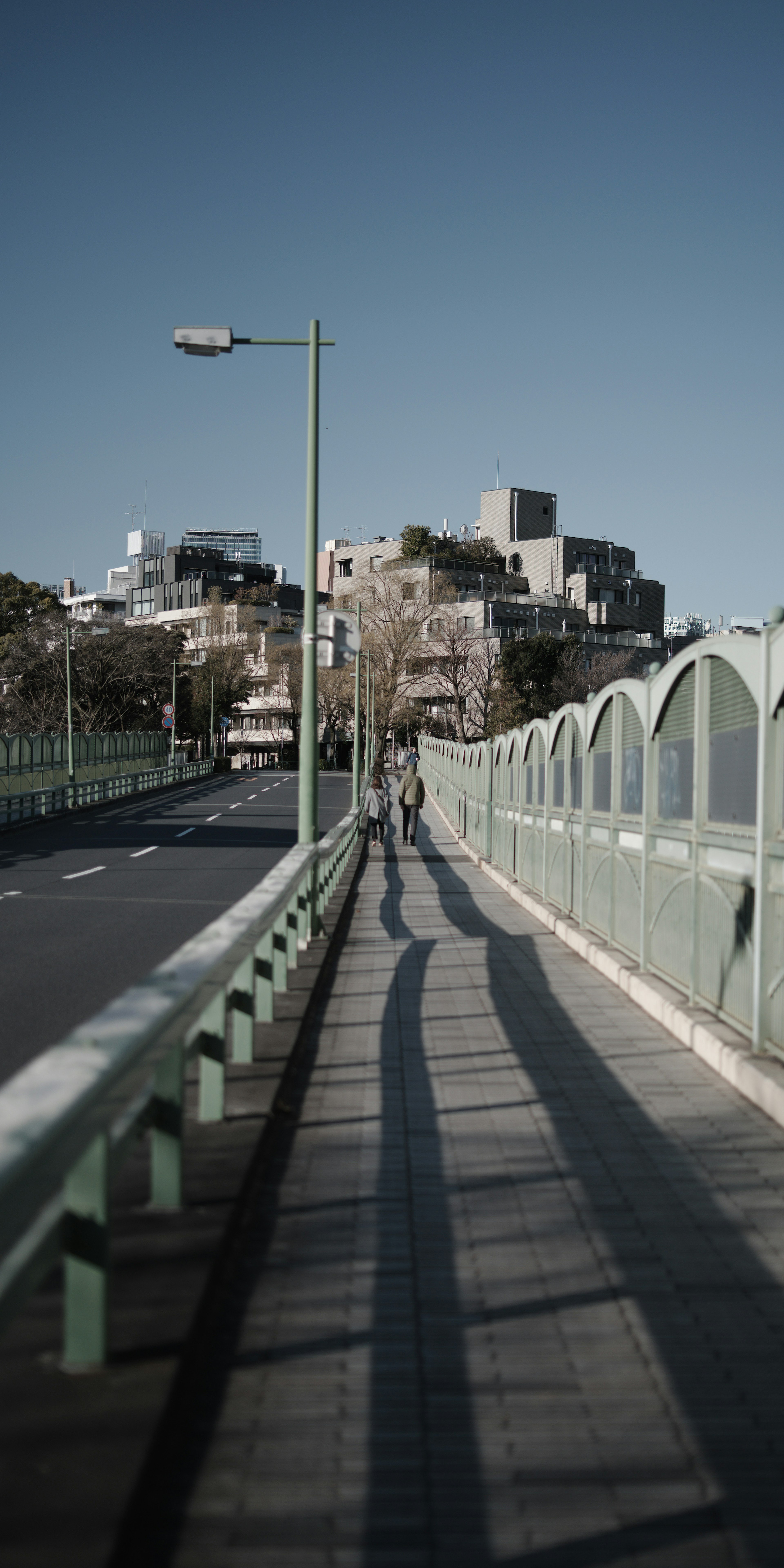 A person walking on a bridge casting long shadows with modern buildings in the background