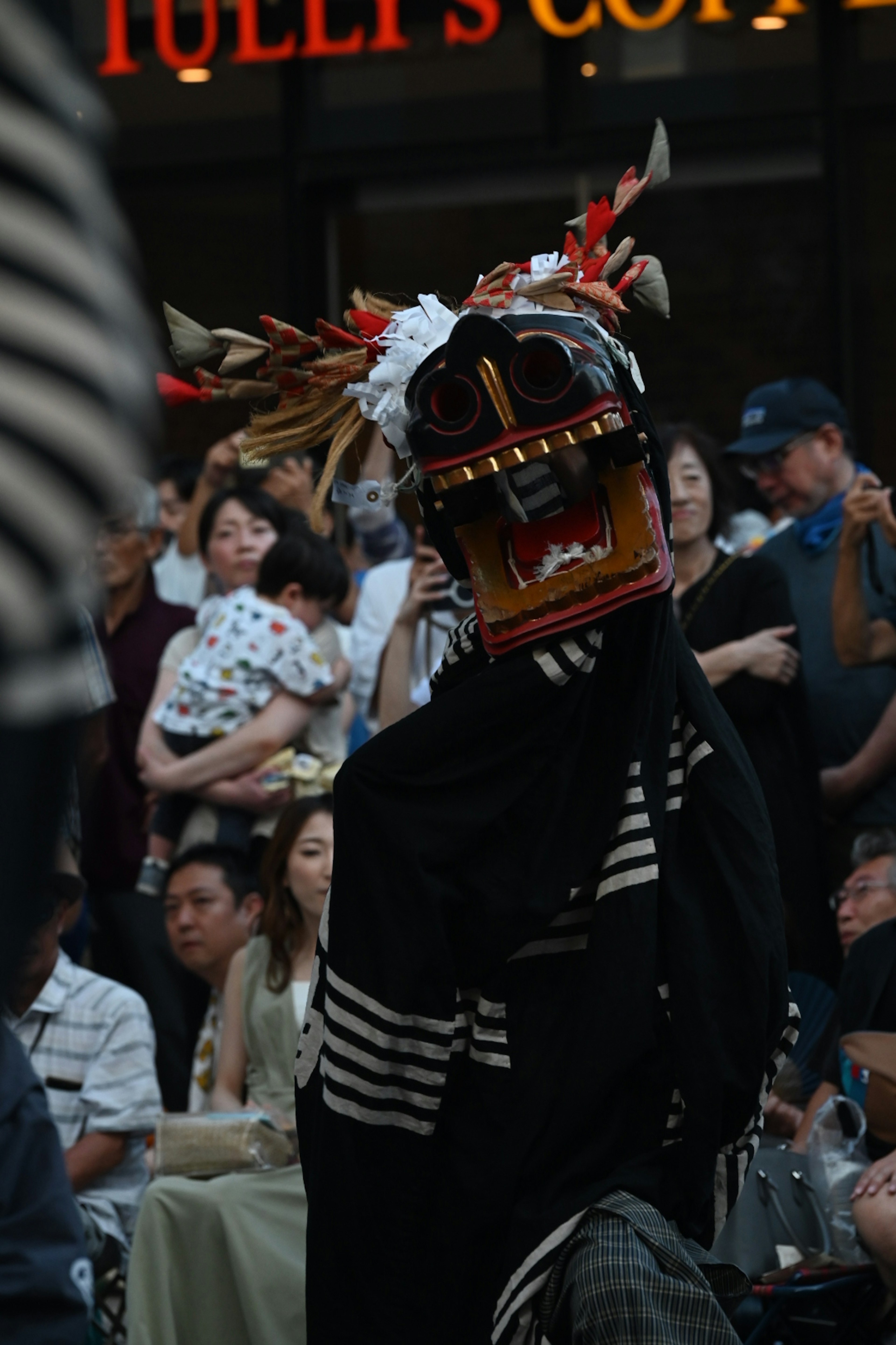 A performer wearing a traditional mask with colorful decorations in front of an audience