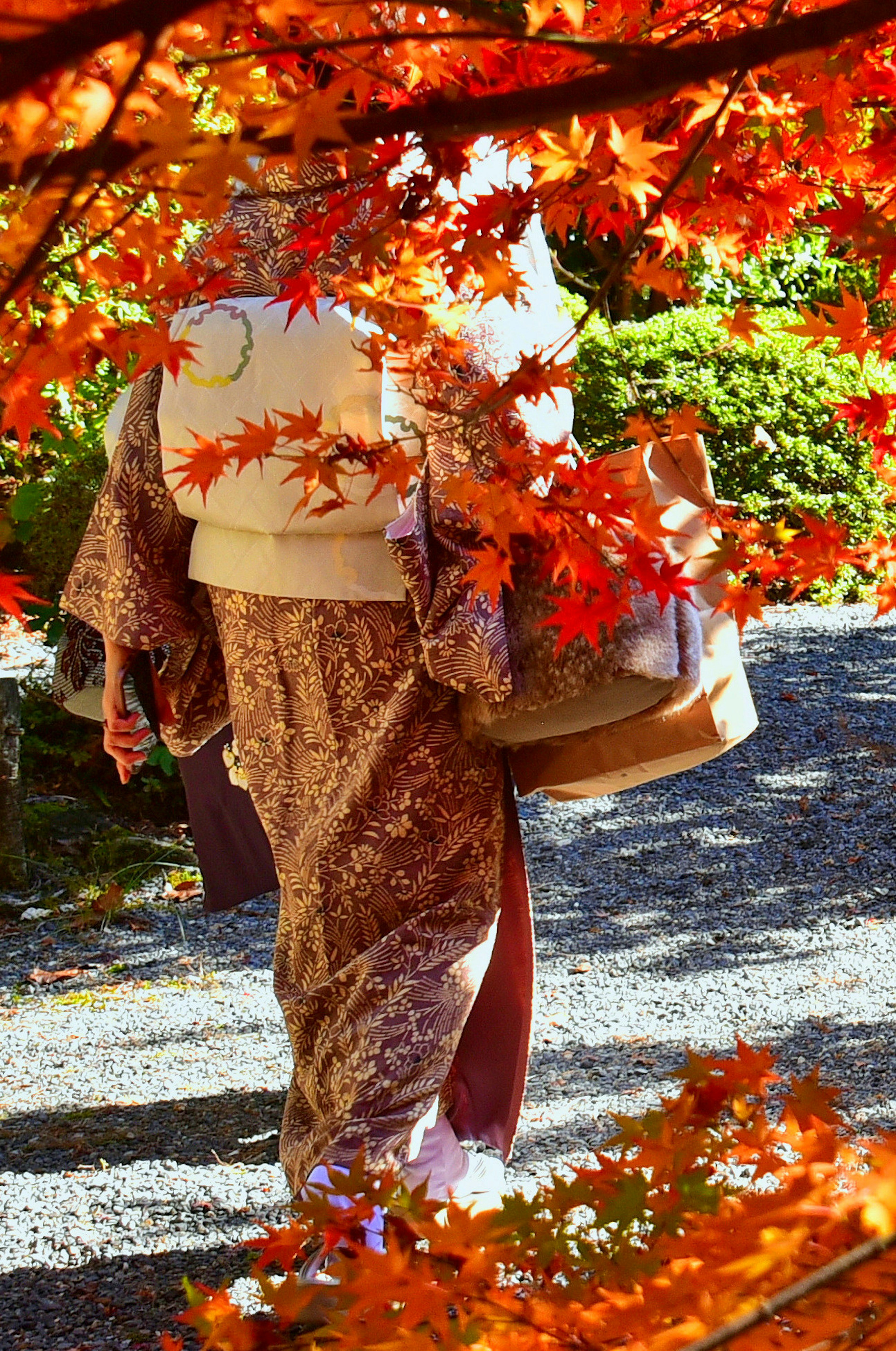 Donna in kimono che cammina tra le foglie autunnali