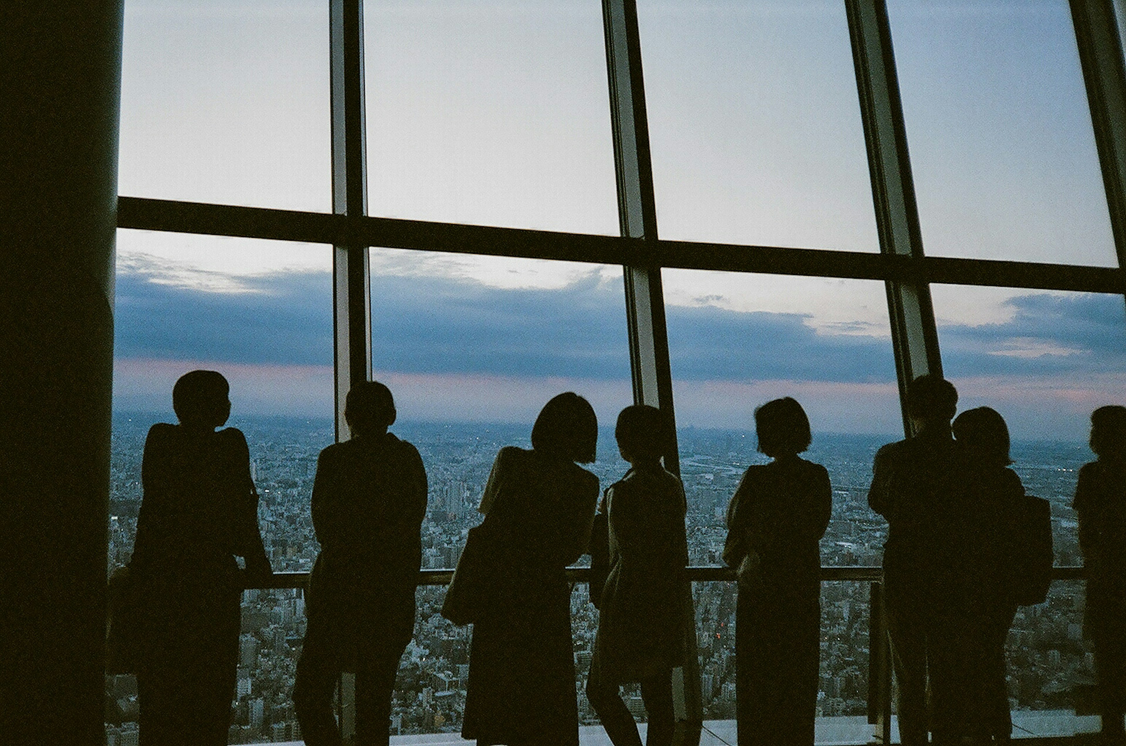 Siluetas de personas de pie junto a una gran ventana con vista a la ciudad