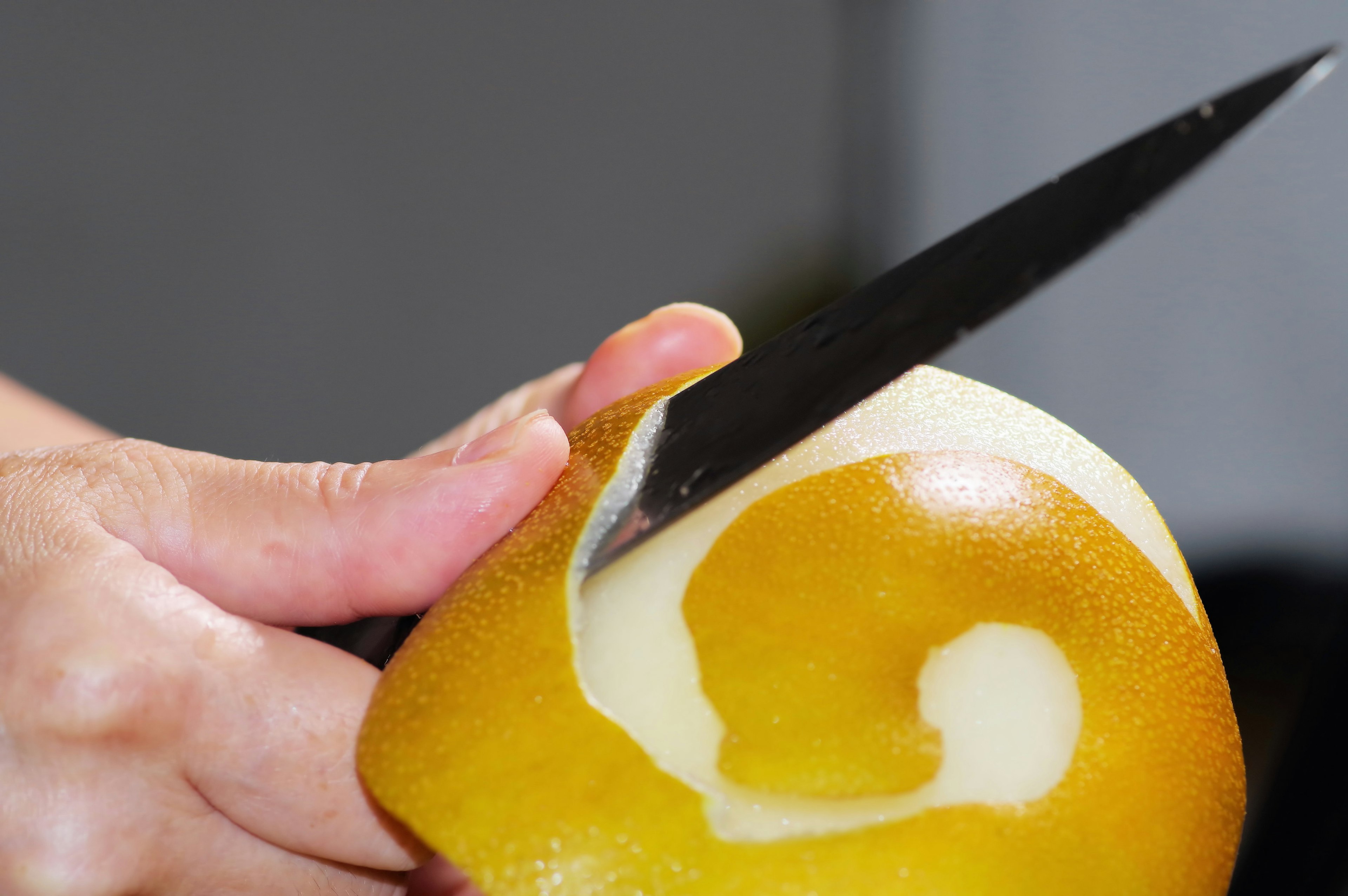 Close-up of hands peeling a fruit creating a spiral pattern with a knife