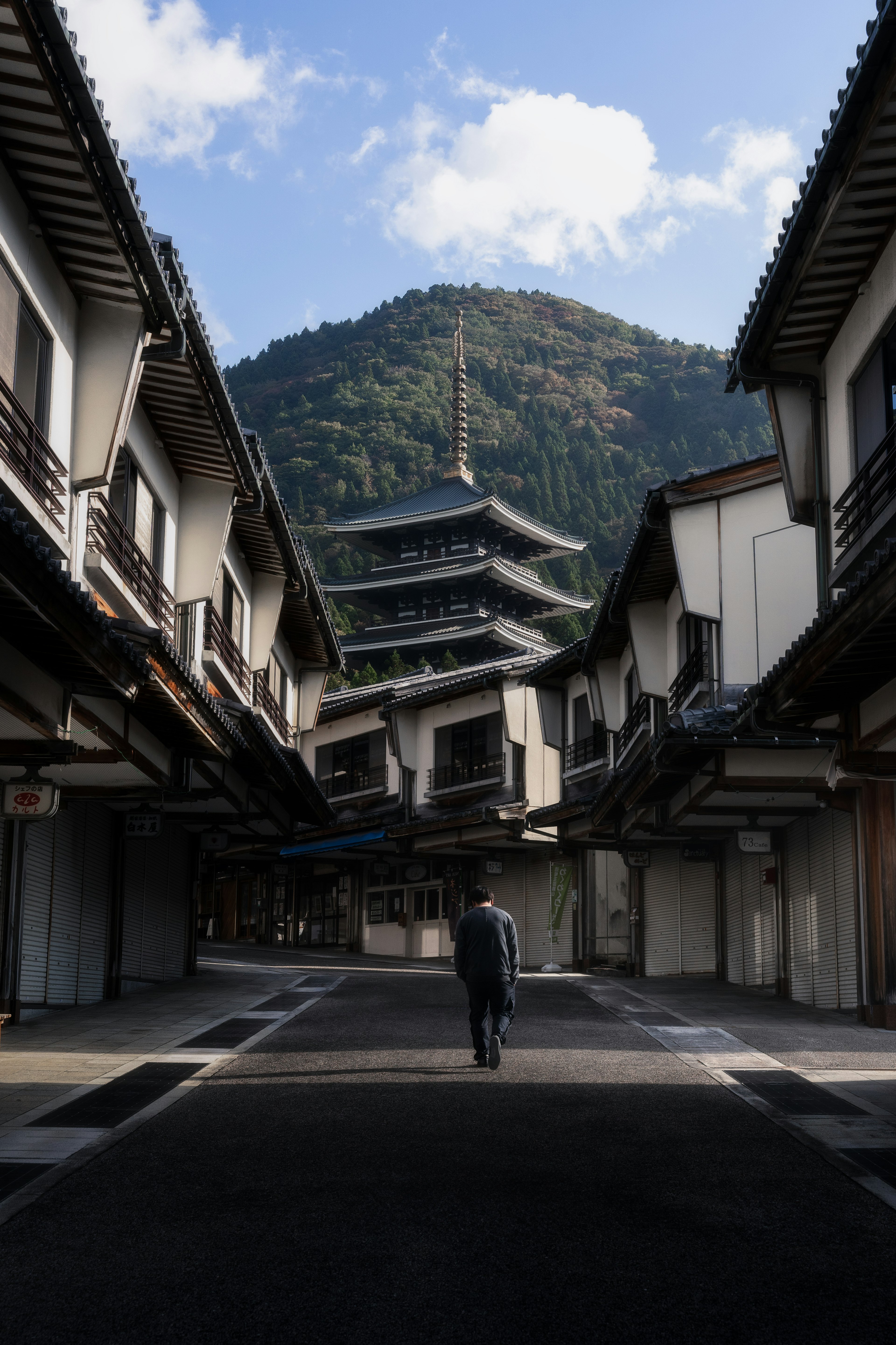 Un hombre caminando por una calle tradicional con una pagoda al fondo