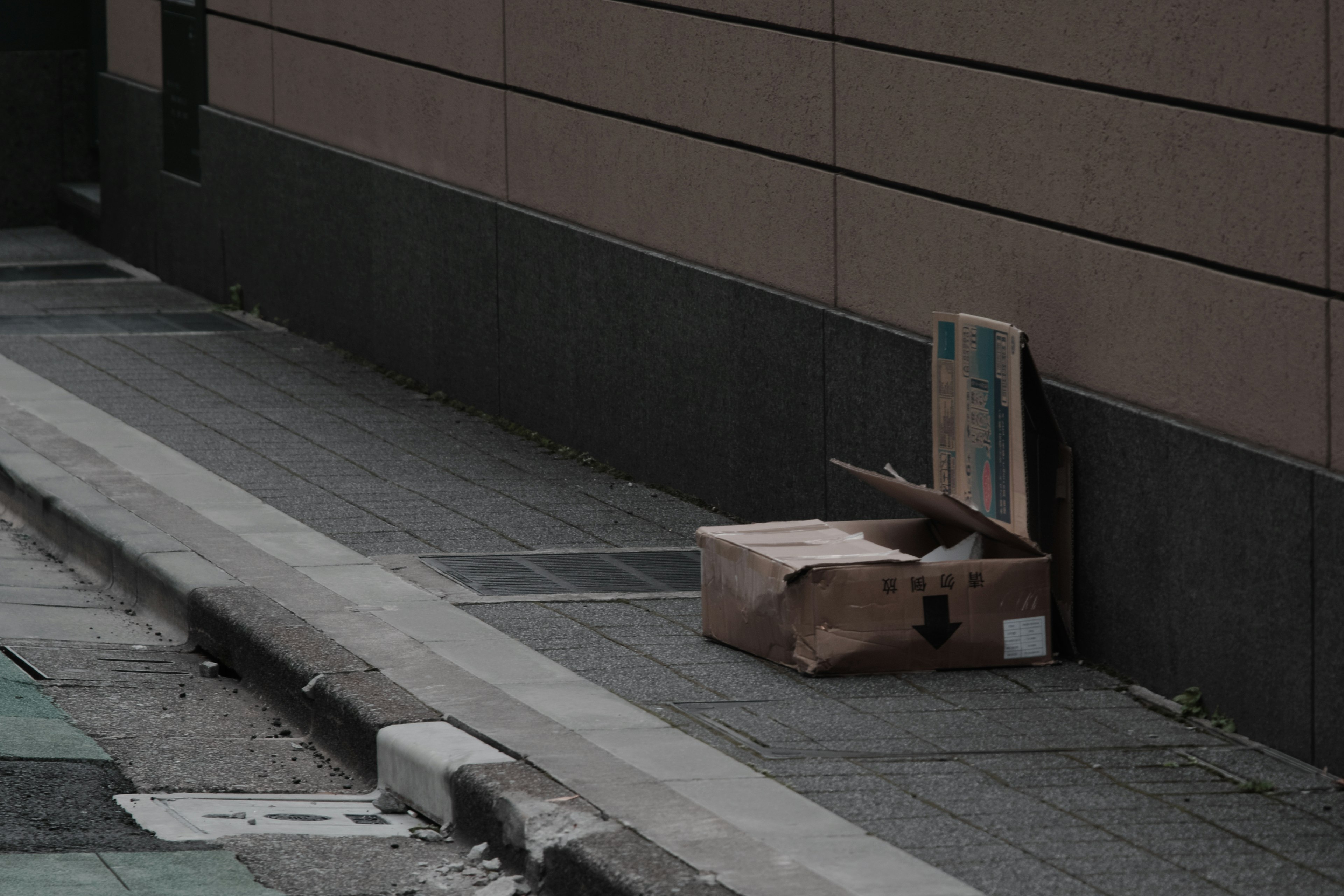 Cardboard box left on the sidewalk next to a wall