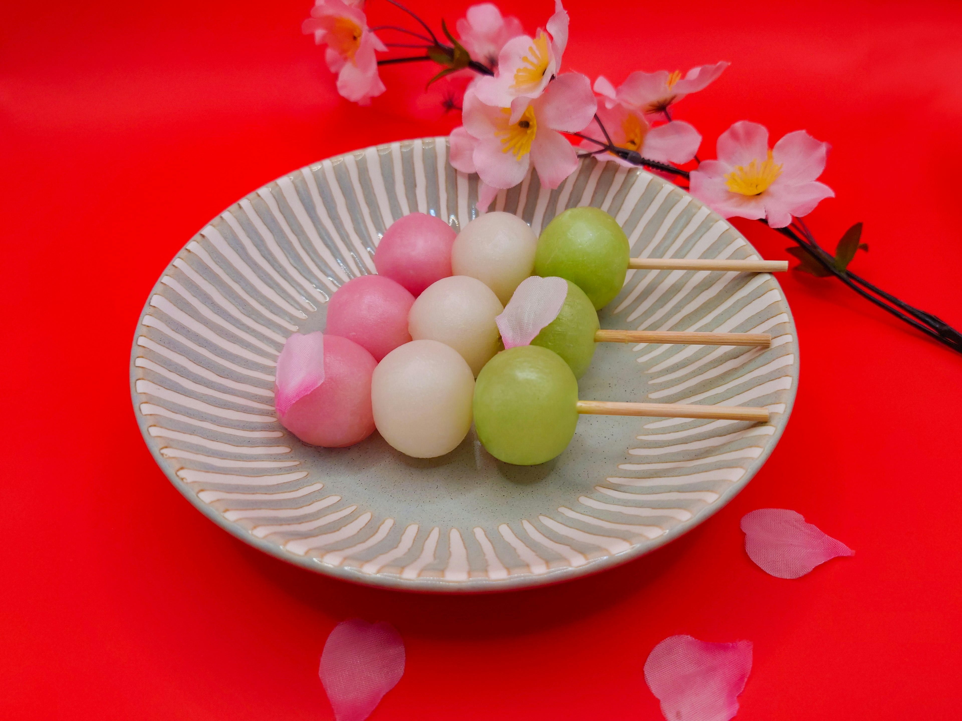 Dango colorido dispuesto en un plato decorativo con flores de cerezo sobre un fondo rojo