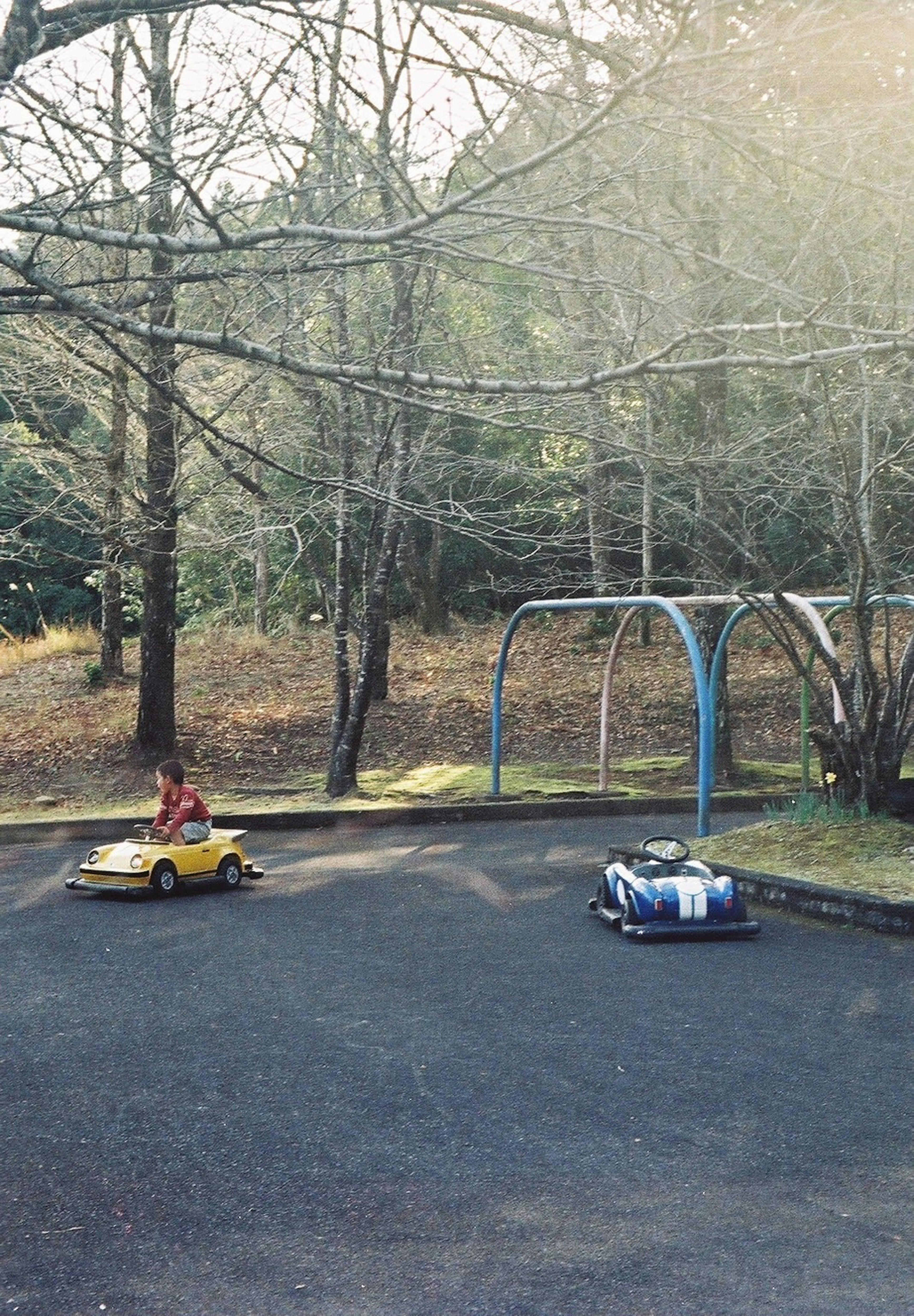 Niños jugando con coches de juguete amarillos y azules en un parque con columpios