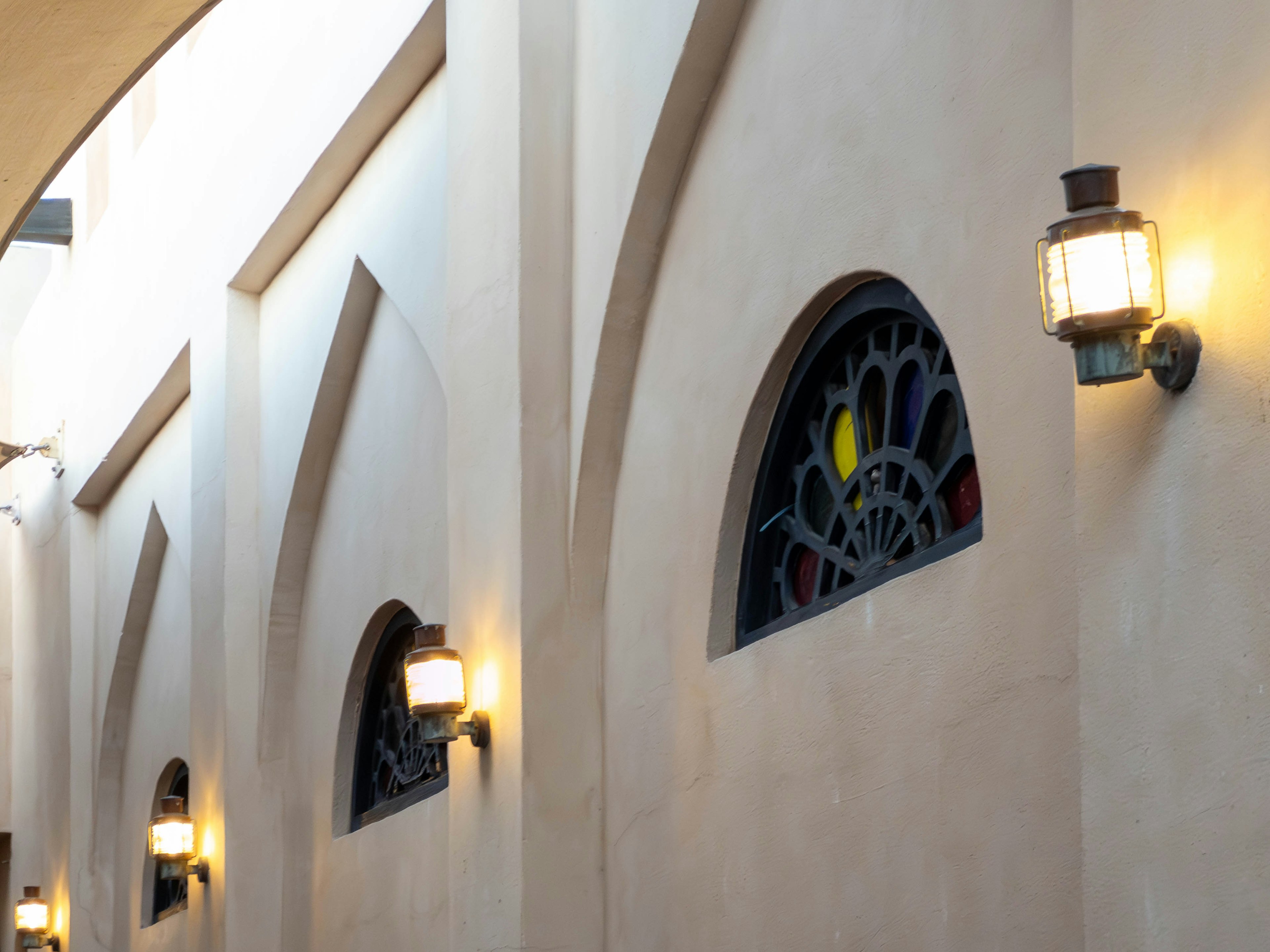 Interior view of an arched hallway with stained glass windows and wall lamps