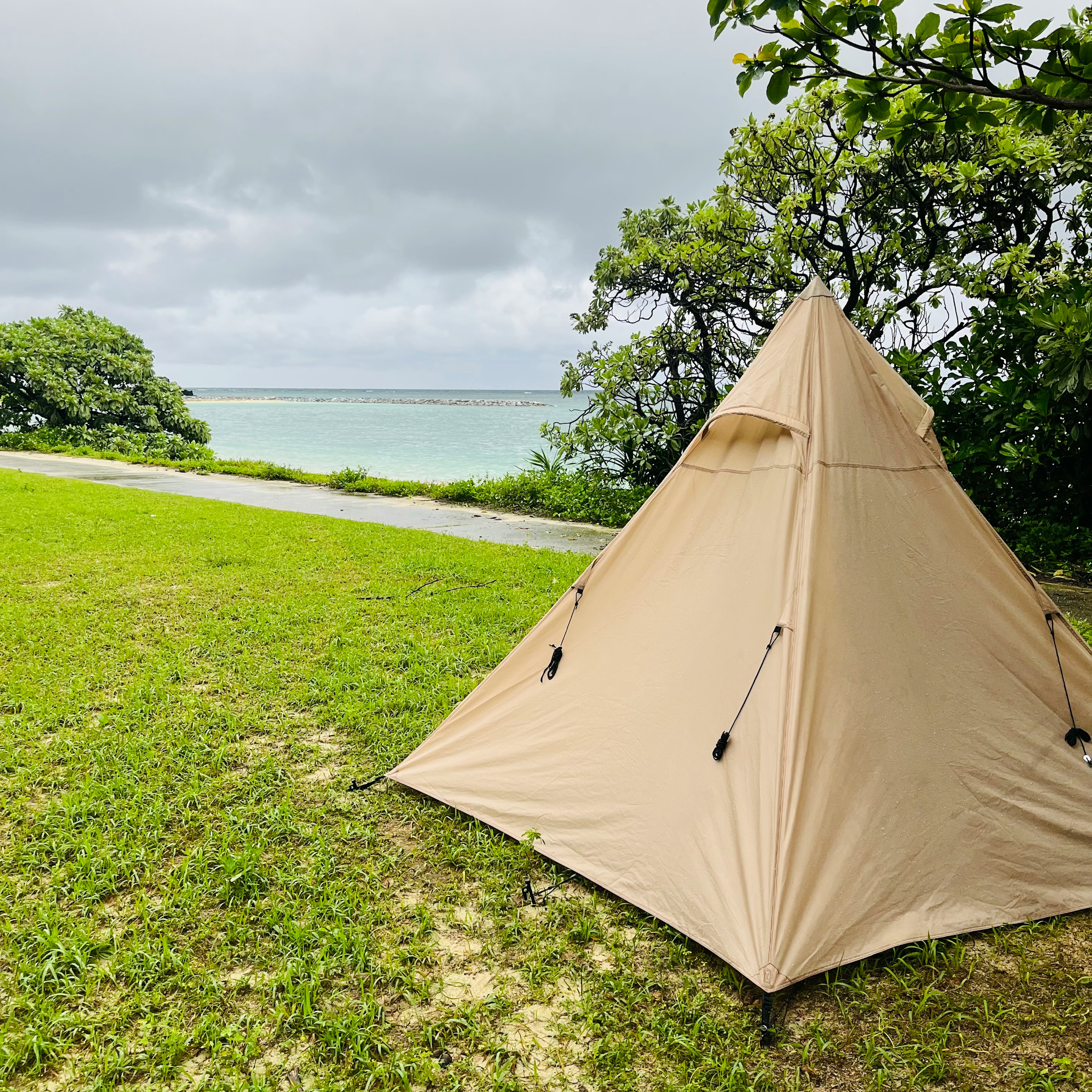 Tenda beige di atas rumput hijau dengan pemandangan laut