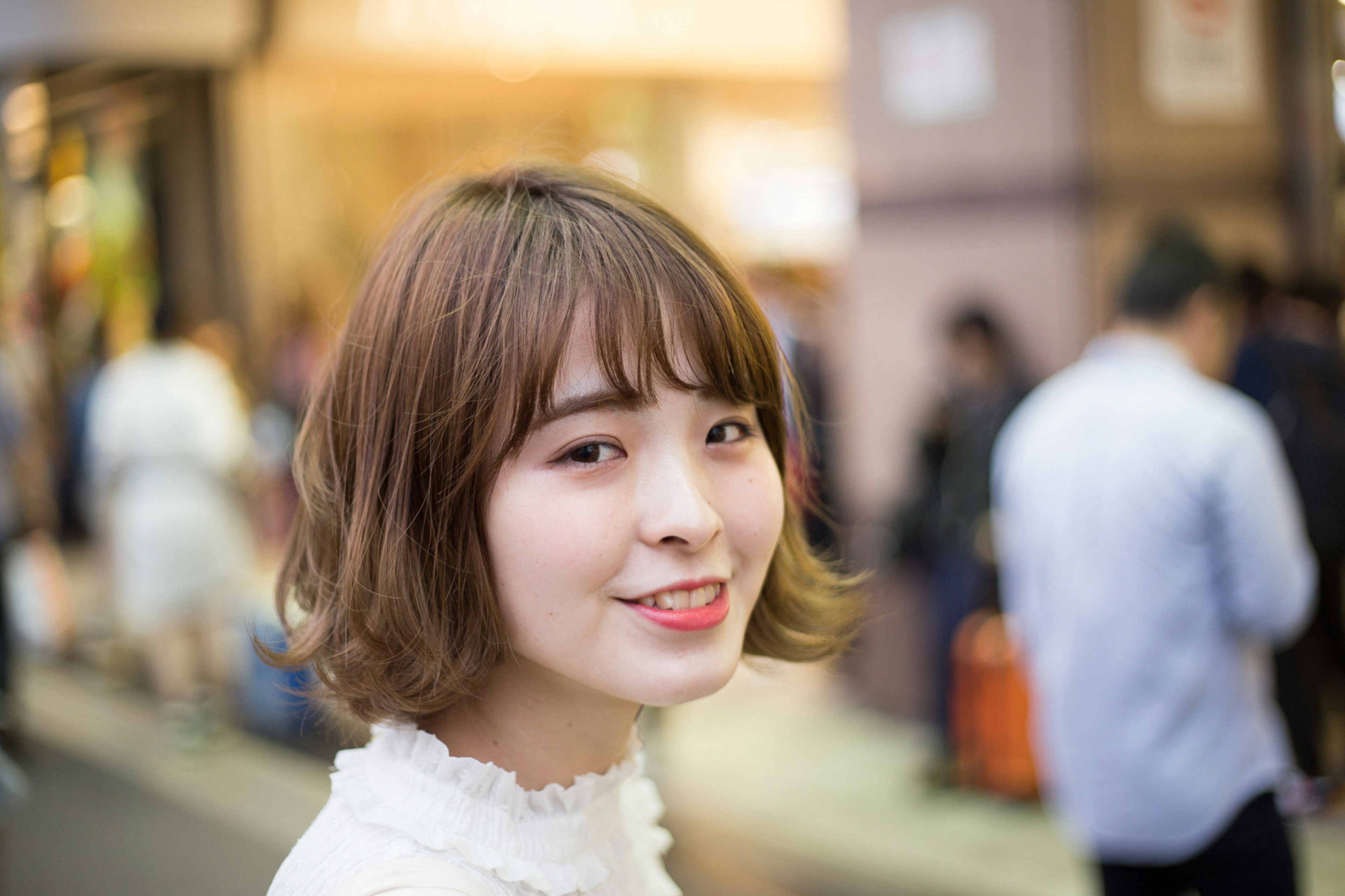 A smiling woman in a street setting with a bright hairstyle and white clothing blurred street background