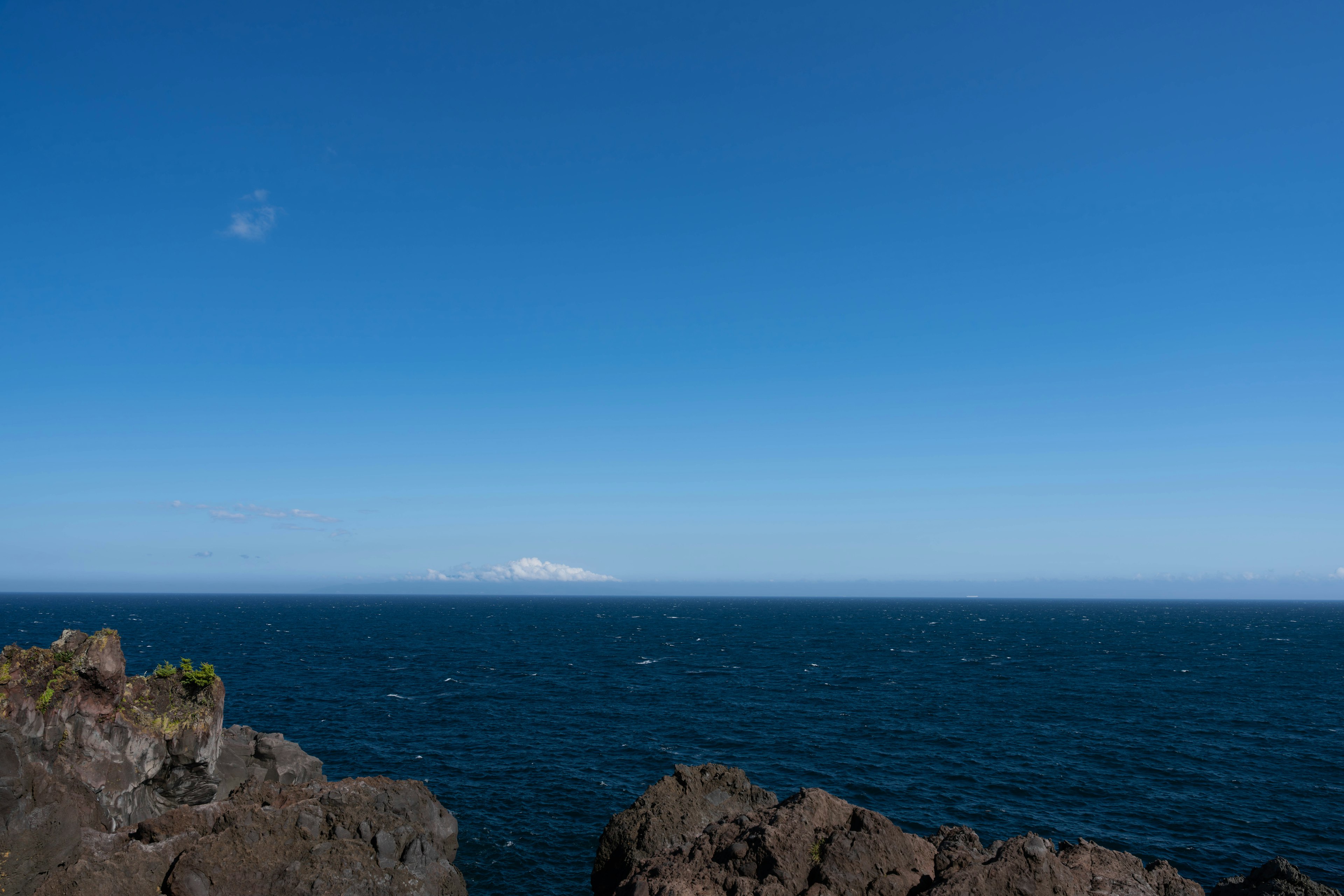 Vista escénica de un cielo azul claro y mar tranquilo con primer plano rocoso